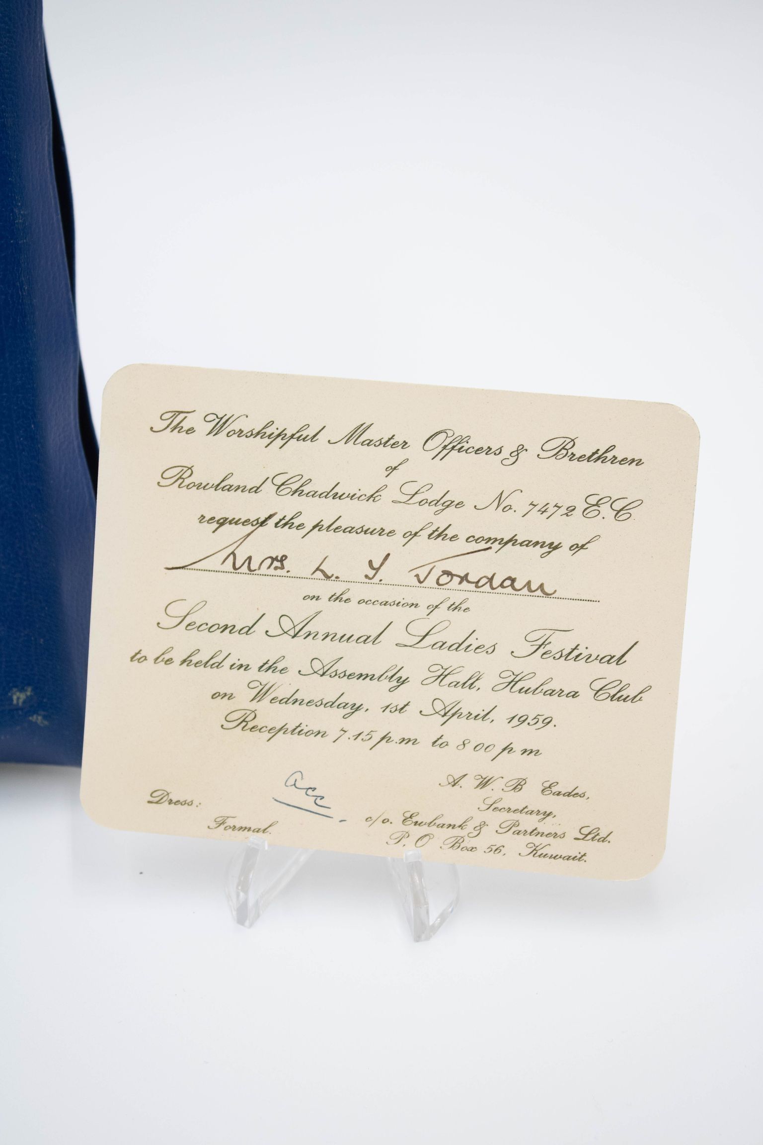 Invitation to the Second Annual Ladies Festival addressed to Mrs. Jessie Jordan.: Image of the cream-colored invitation with black cursive text. The invitation reads "The Worshipful Master Officers of Brethren of Rowland Chadwick Lodge No. 7472 E.C. request the pleasure of the company of Mrs. L.T. Jordan on the occasion of the Second Annual Ladies Festival to be held in the Assembly Hall, Hubara Club on Wednesday, 1st April, 1959. Reception 7:45 p.m. to 8 p.m." in the center. In the bottom left, it reads "Dress: Formal" and in the bottom right, it reads "A.W.B Eades, Secretary, c/o. Eubank & Partners Ltd., P.O Box 56, Kuwait."