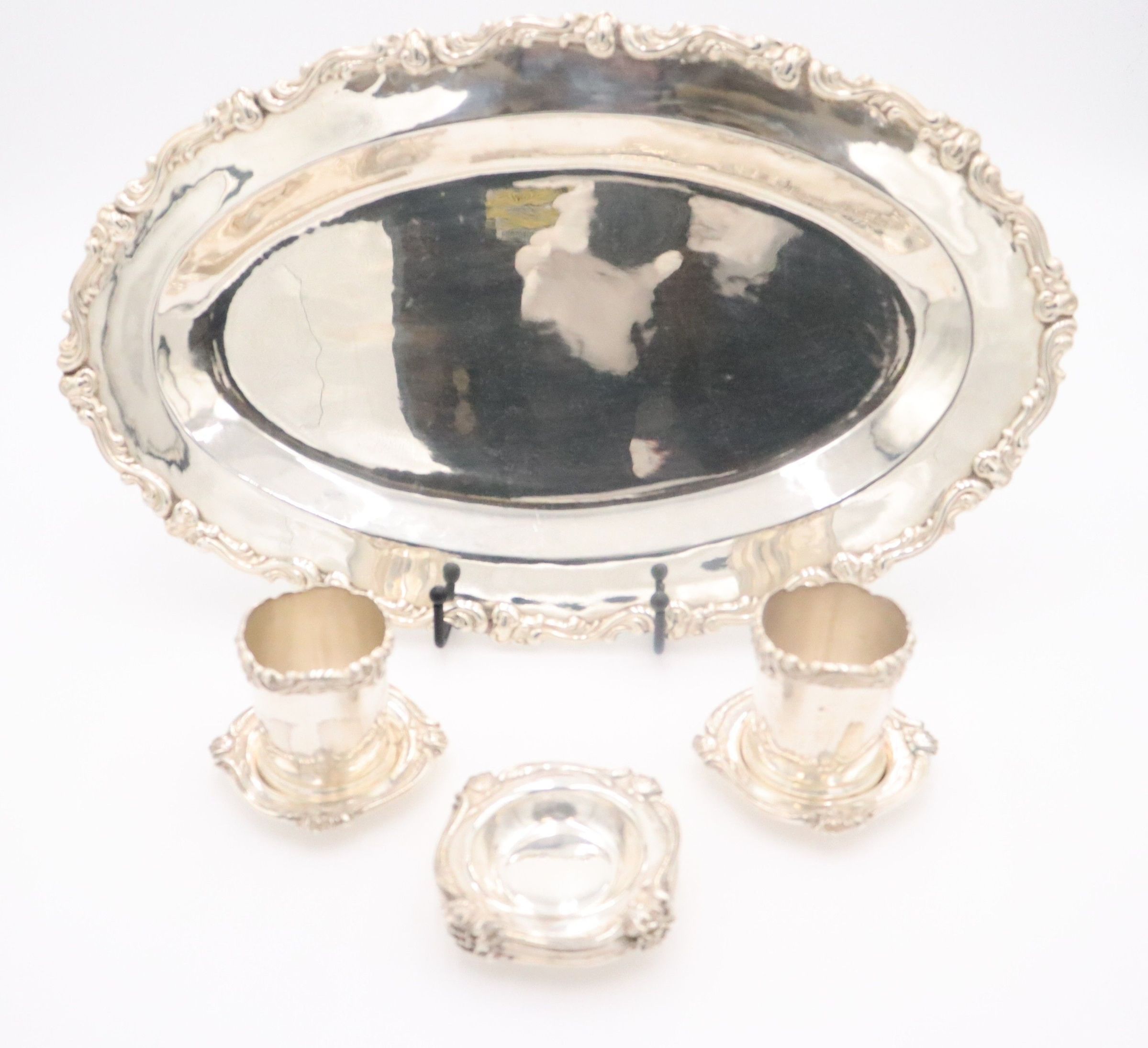 Full set of Salver, Cups, and Saucers: Image showing the full set of the silver salver, two cups, and six saucers. The salver is oval-shaped and is edged with a scroll design. It is flat and has a divot for the saucers and cups. The six saucers are on the salver, as well as the cups which are on top of two saucers.
