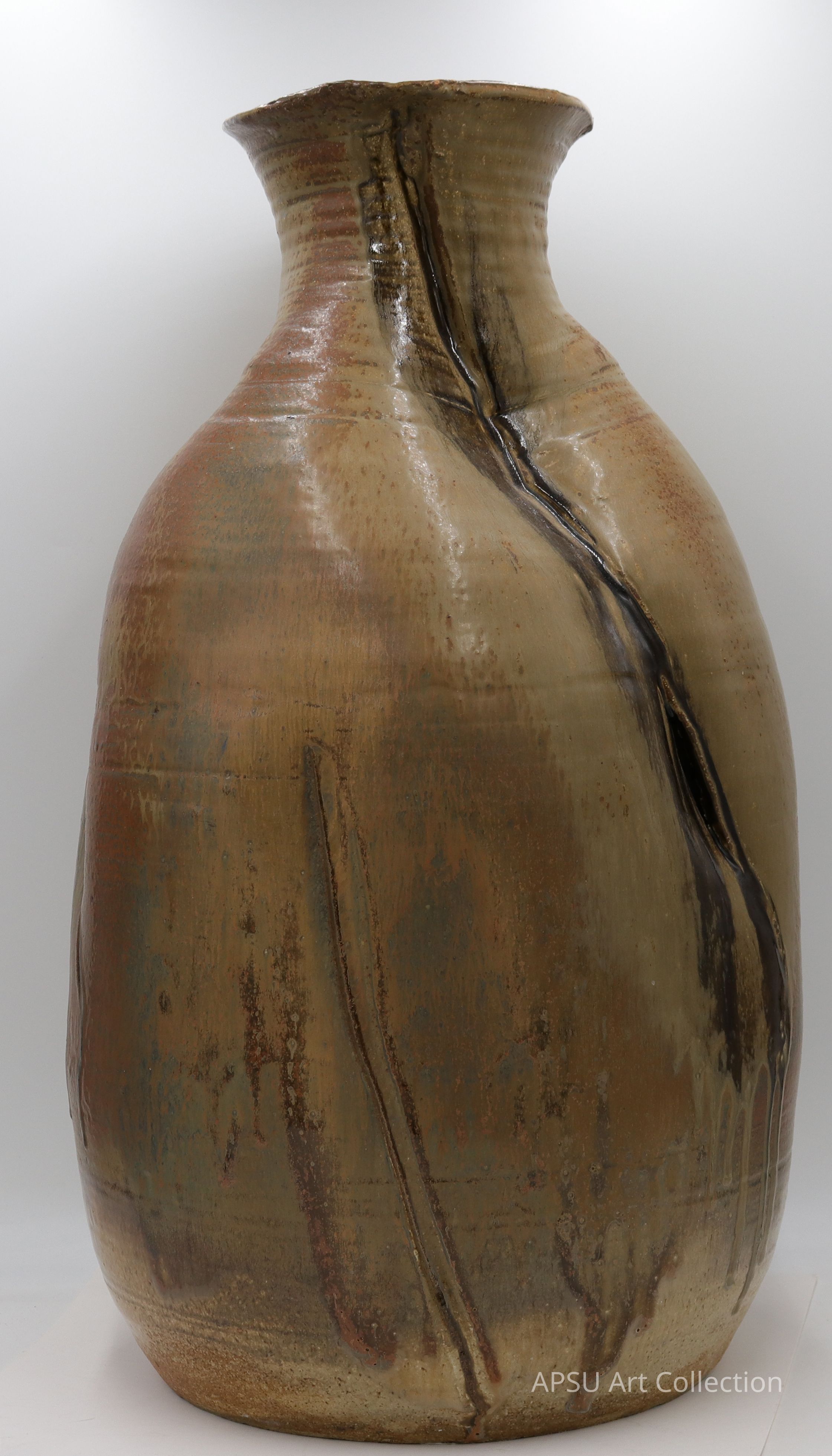 The image showcases a large, elegant ceramic vase with a high-gloss finish, featuring a smooth, rounded body that tapers into a narrower neck; the surface displays a blend of earthy tones, including subtle browns and muted blues, with distinct vertical streaks adding texture and character, while the vase stands on a simple, slightly rounded base, and the background is a soft, textured beige, which enhances the natural hues of the piece, creating a harmonious visual effect that emphasizes the artisanal craftsmanship.