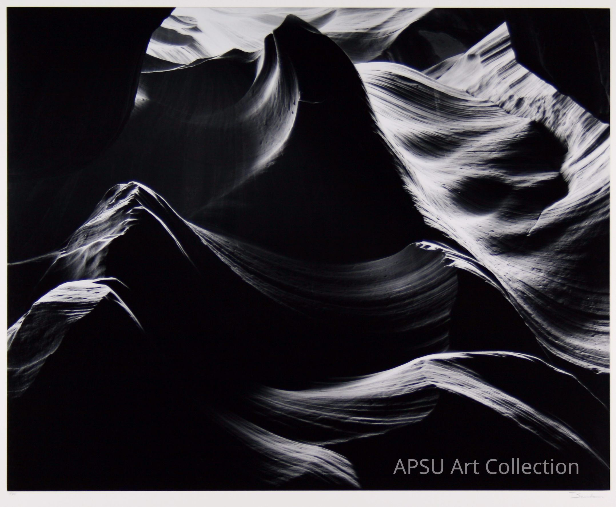 The image depicts a stunning, black and white photograph of an abstract rock formation with smooth, flowing lines and intricate textures, illuminated dramatically by light falling from above, creating a stark contrast between the dark shadows and bright highlights, capturing the ethereal beauty of the natural landscape in a mesmerizing and almost surreal manner.
