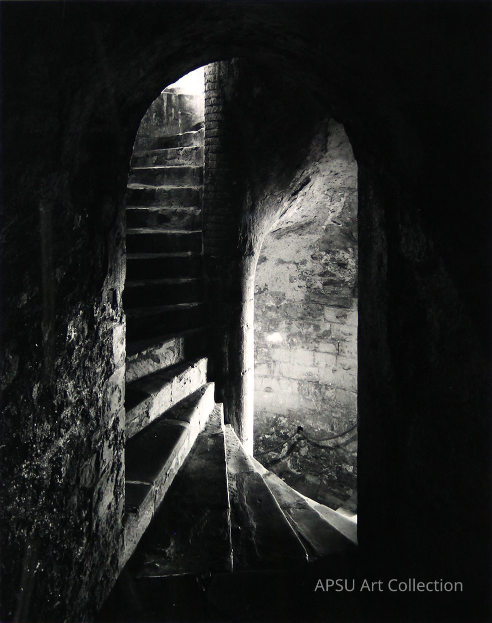 The image encapsulates a captivating monochromatic shot of an ancient, possibly medieval, stone architecture featuring a flight of stone stairs ascending through a dark passage illuminated intermittently by the soft light filtering in from arched openings, casting an enigmatic allure through light and shadow play, evoking a sense of historical depth and the mystery of the passage of time.