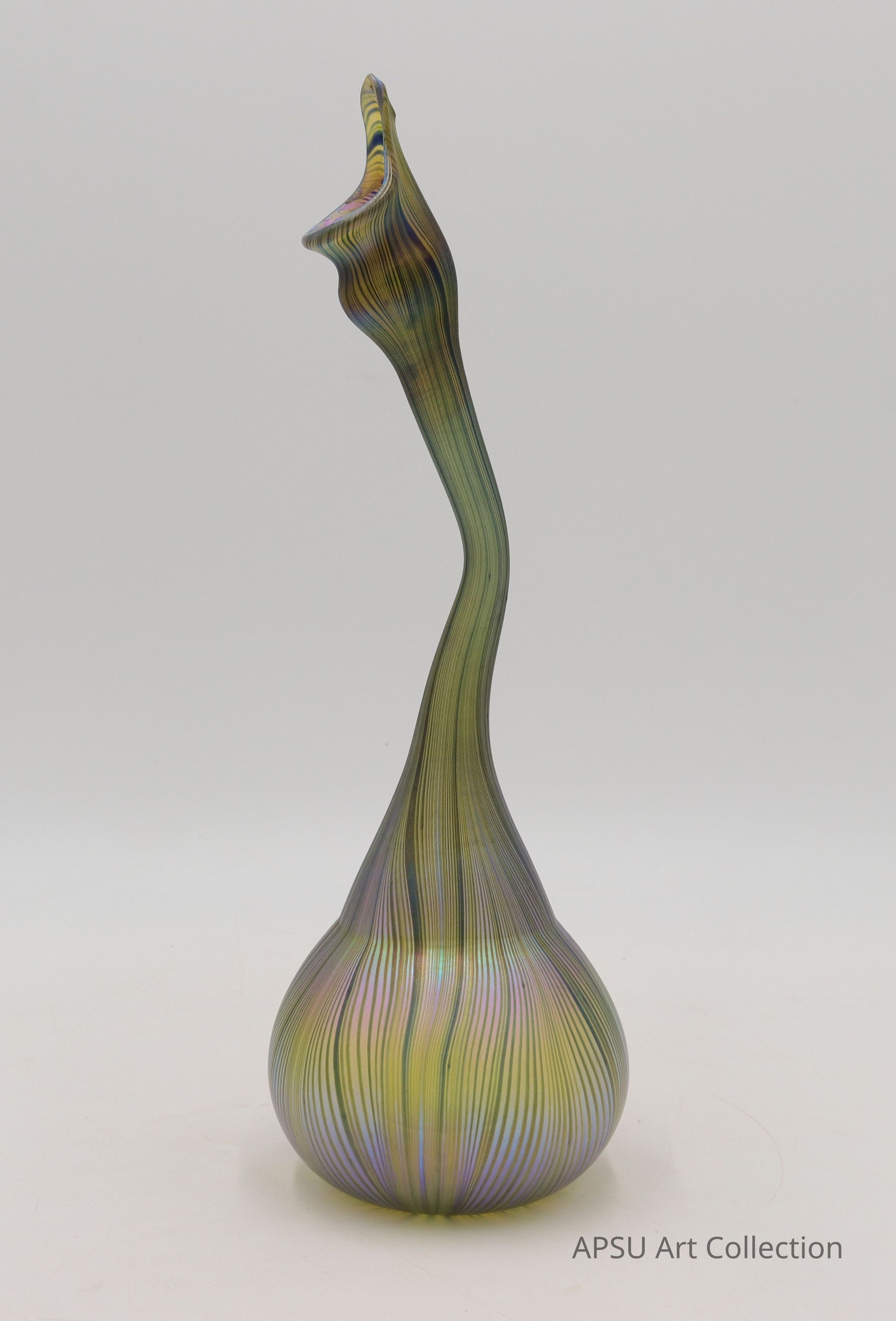 The image showcases an elegantly crafted glass sculpture resembling a twisted, elongated bottle with an iridescent finish that reflects various shades of green, yellow, and purple, giving it a mystical and otherworldly appearance; its curvaceous form rises gracefully from a bulbous base, tapering into a narrow, whimsically bent neck, suggesting both fluidity and tension, while the delicate stripes enhance its textural complexity, inviting observers to appreciate the blend of artistry and craftsmanship embodied in the object, as set