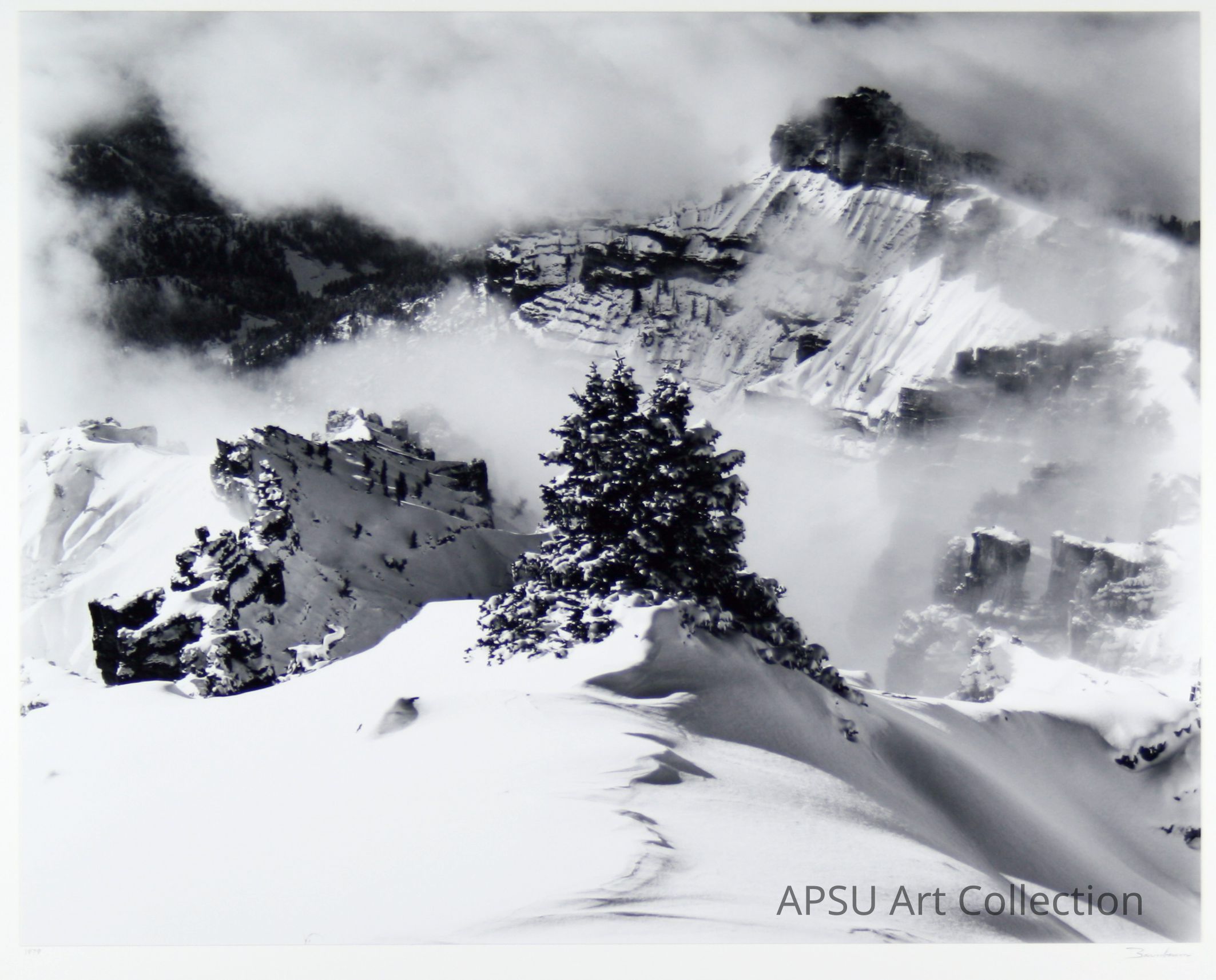 The black and white photograph captures a breathtaking winter landscape, showcasing majestic, snow-covered mountain cliffs shrouded in swirling mist, with a solitary, frost-laden tree standing prominently in the foreground, evoking a sense of solitude, tranquility, and the raw beauty of untouched nature.
