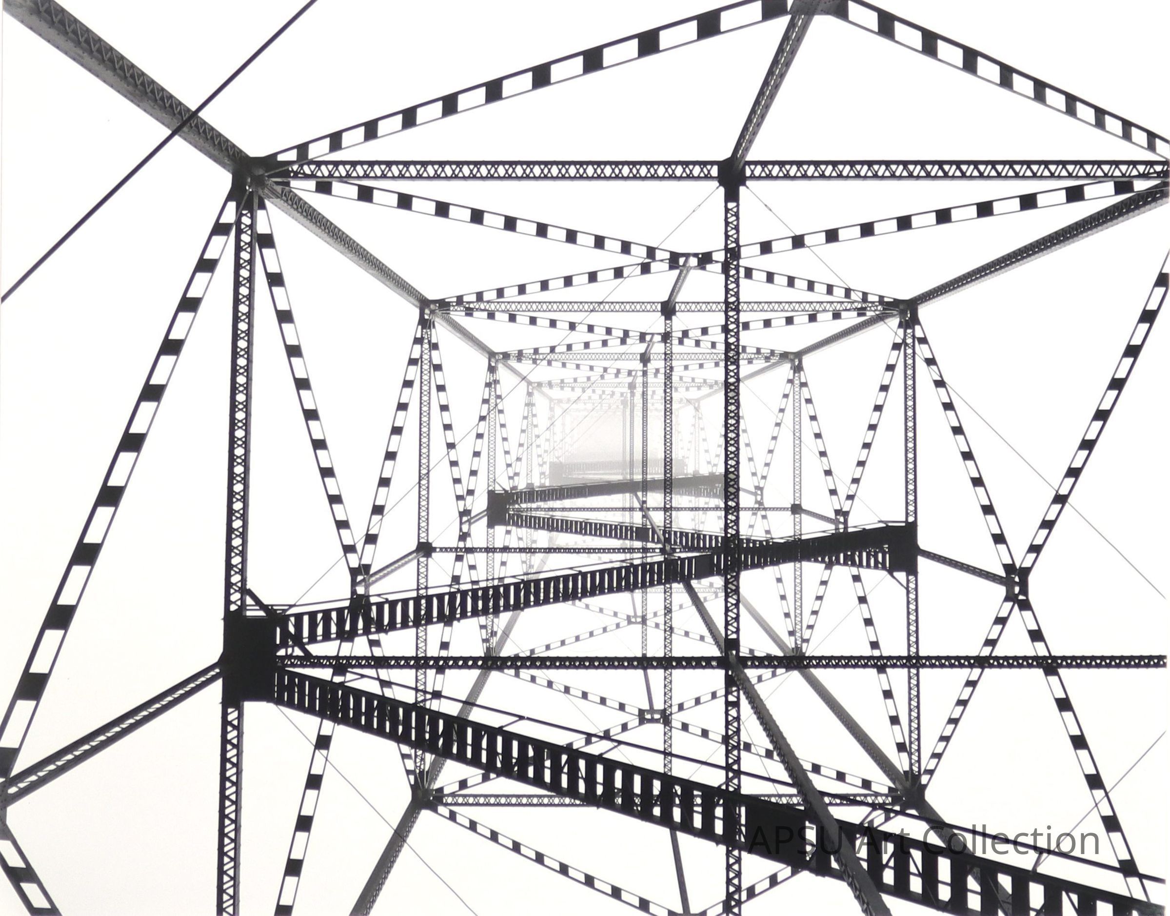 This image captures the intricate geometric structure of a metal tower, showcasing a complex network of beams and connections that form a lattice pattern. The symmetrical viewpoint looking up inside the tower emphasizes the engineering precision and repetitive beauty of industrial construction. The monochrome color scheme enhances the stark contrasts created by the beams, which fade into a vanishing point at the center, surrounded by a hazy, overcast sky. The photo's composition highlights the strength and durability inherent in such man-made structures.