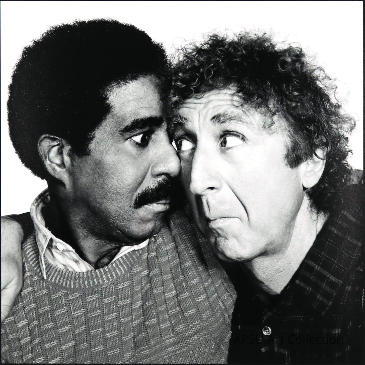 This black and white photograph captures a humorous and expressive moment between two men, where one with a curly mop of hair and crinkled eyes is humorously gawking at the other, a man with a neat afro, whose expression is one of mild amusement and surprise. They appear intimately close, indicating a moment of playful interaction, set against a plain background that enhances their vivid facial expressions and the stark contrast in their features.