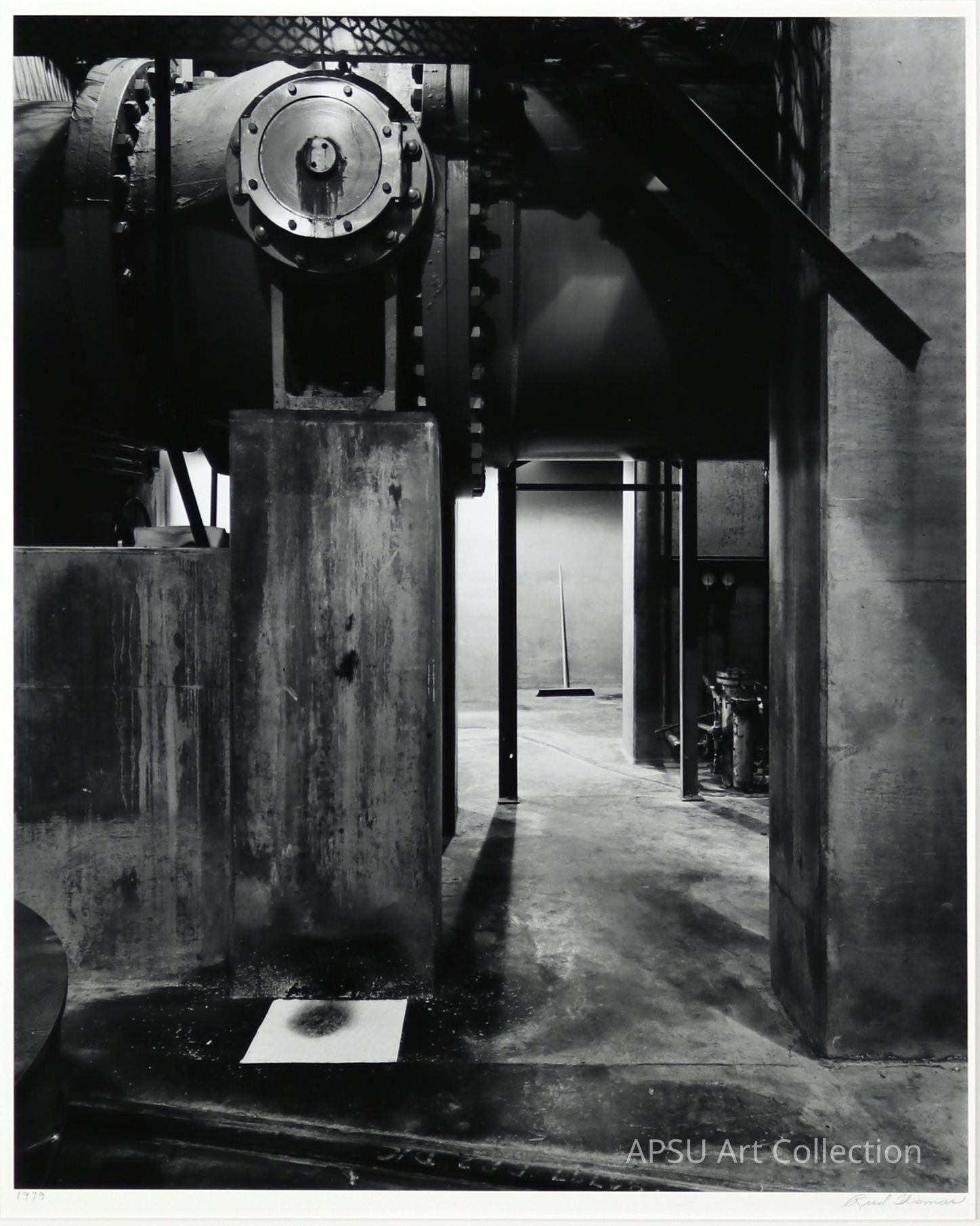 The image displays a stark, industrial scene, primarily in shades of gray, featuring robust machinery components with intricate textures and visible bolts. At the forefront, there are stark concrete supports, weathered, indicating age or exposure to harsh conditions. Shadows cast across the floor contribute to the moody, somewhat desolate atmosphere of the setting. A subtle highlight is a lone push broom seemingly misplaced or forgotten in the industrial environment, adding mystery to the photo's narrative.
