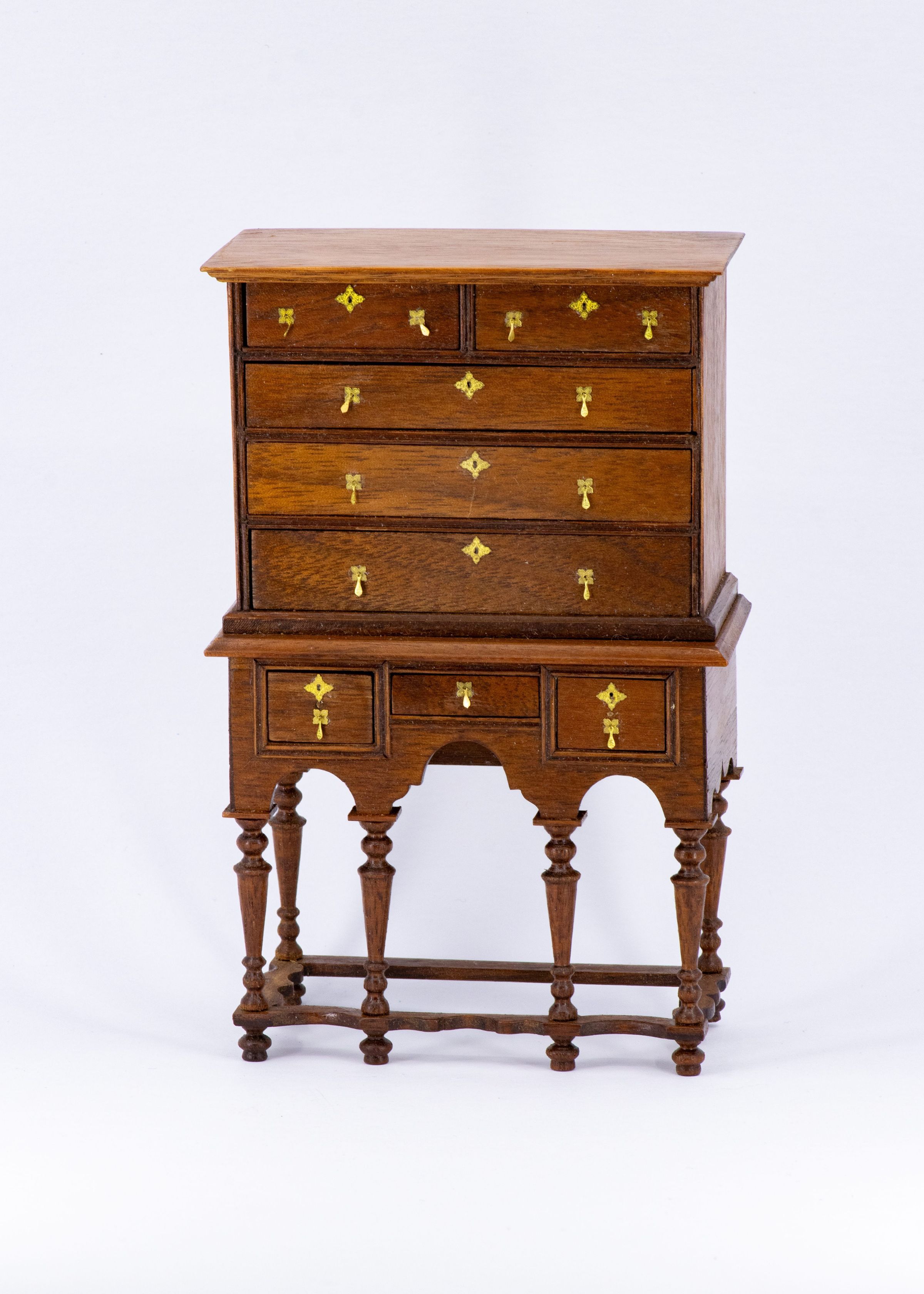 A tall wooden dresser: An ornate, antique wooden dresser with 5 rows of drawers - the topmost divided in two while the next three long across the body. The last row is separated by trim and divided into 3 smaller drawers. All drawers are decorated with brass handles and the dresser sits on tall, intricately carved legs.