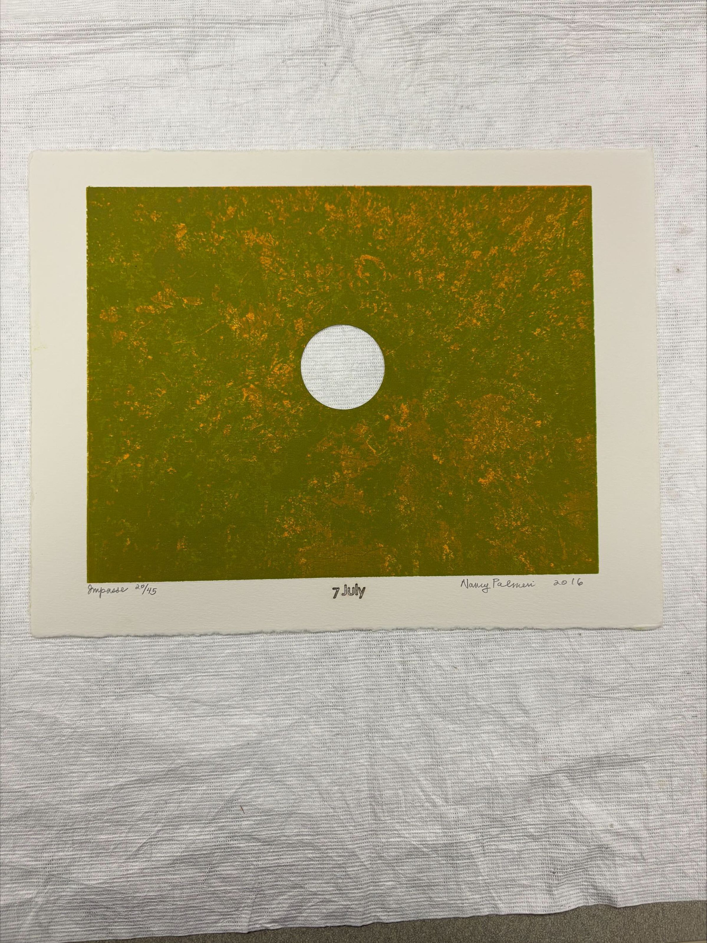 Front: A horizontal oriented, standard letter size relief print with colors of green, orange and yellow. The print has a hole cut out in the center and is an abstract application of ink onto paper.