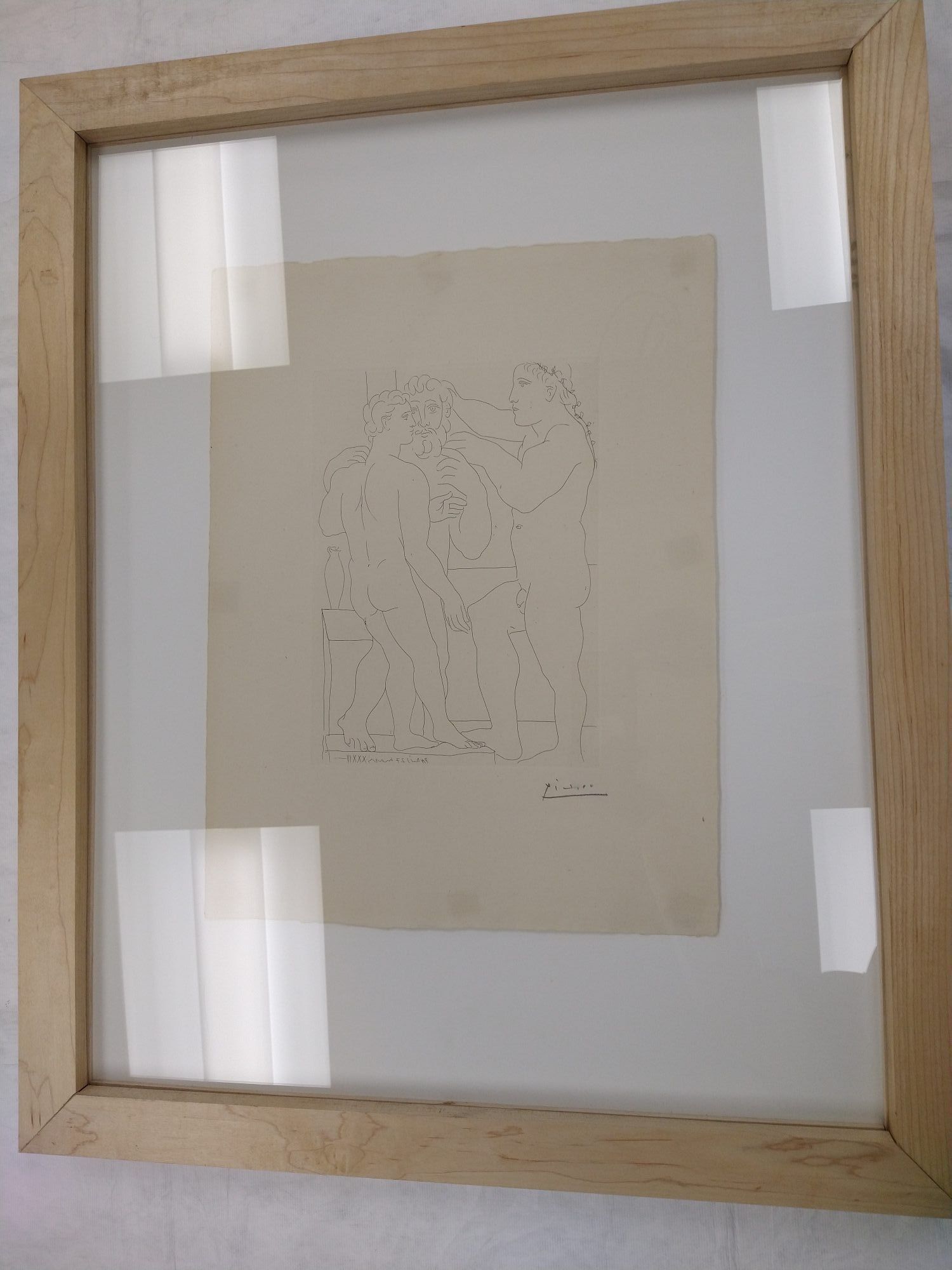 Deux Hommes Sculptés (Three Nude Men Standing): Medium artwork of three nude men standing and facing each other. Behind the far left figure is an outline of a table with a vase sitting on it. The far-right figure is wearing a vine headband that drapes down his back. Two outer figures are facing each other, while the middle figure is facing straight on. The print is displayed in a wood frame.