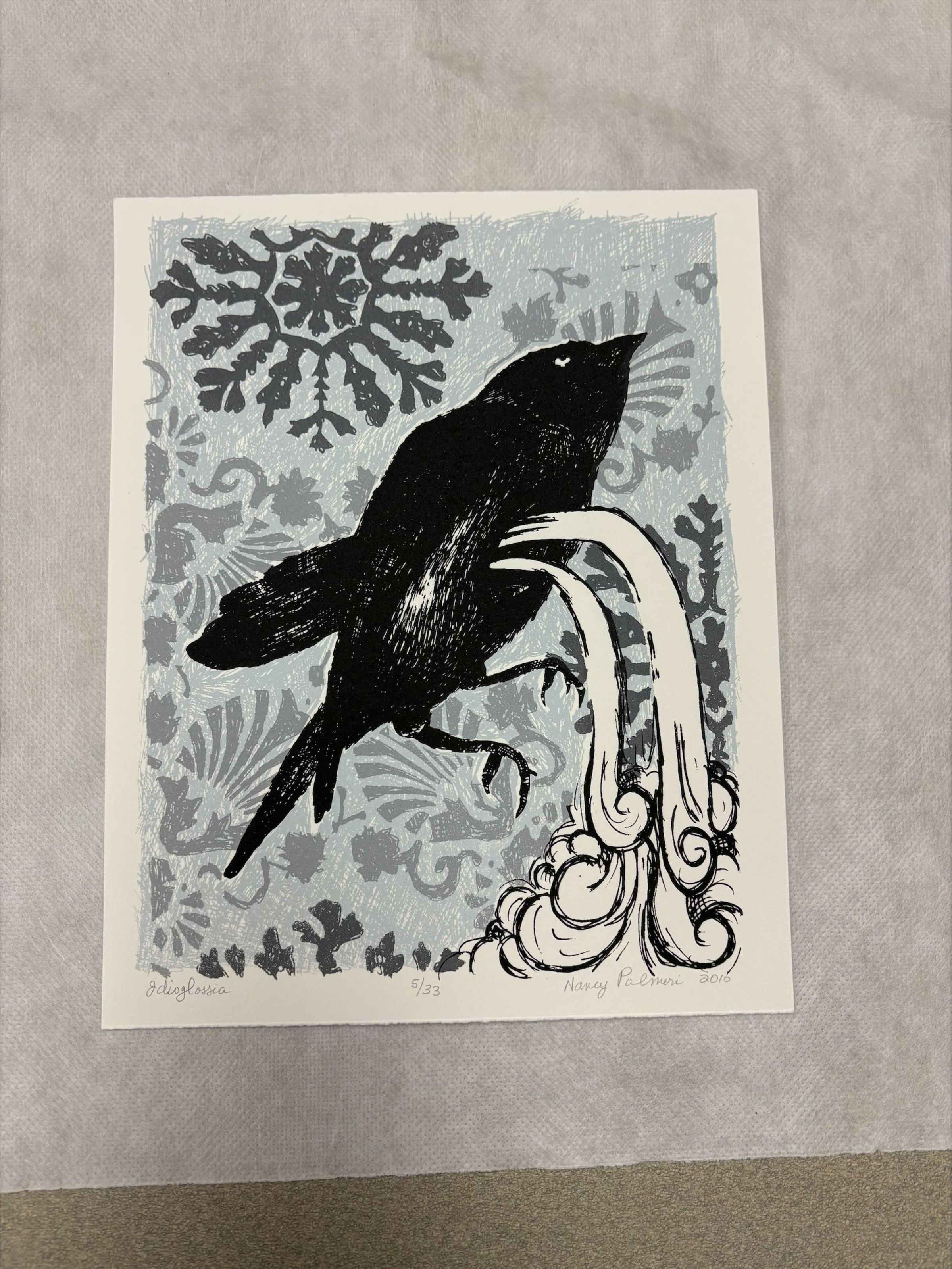 Front: A vertically oriented, medium sized print that uses blue, black, white and shades of grey to create the image. The central form is that of a bird with a stream like detail flowing out from its side, while surrounded by floral and snowflake like patterns.