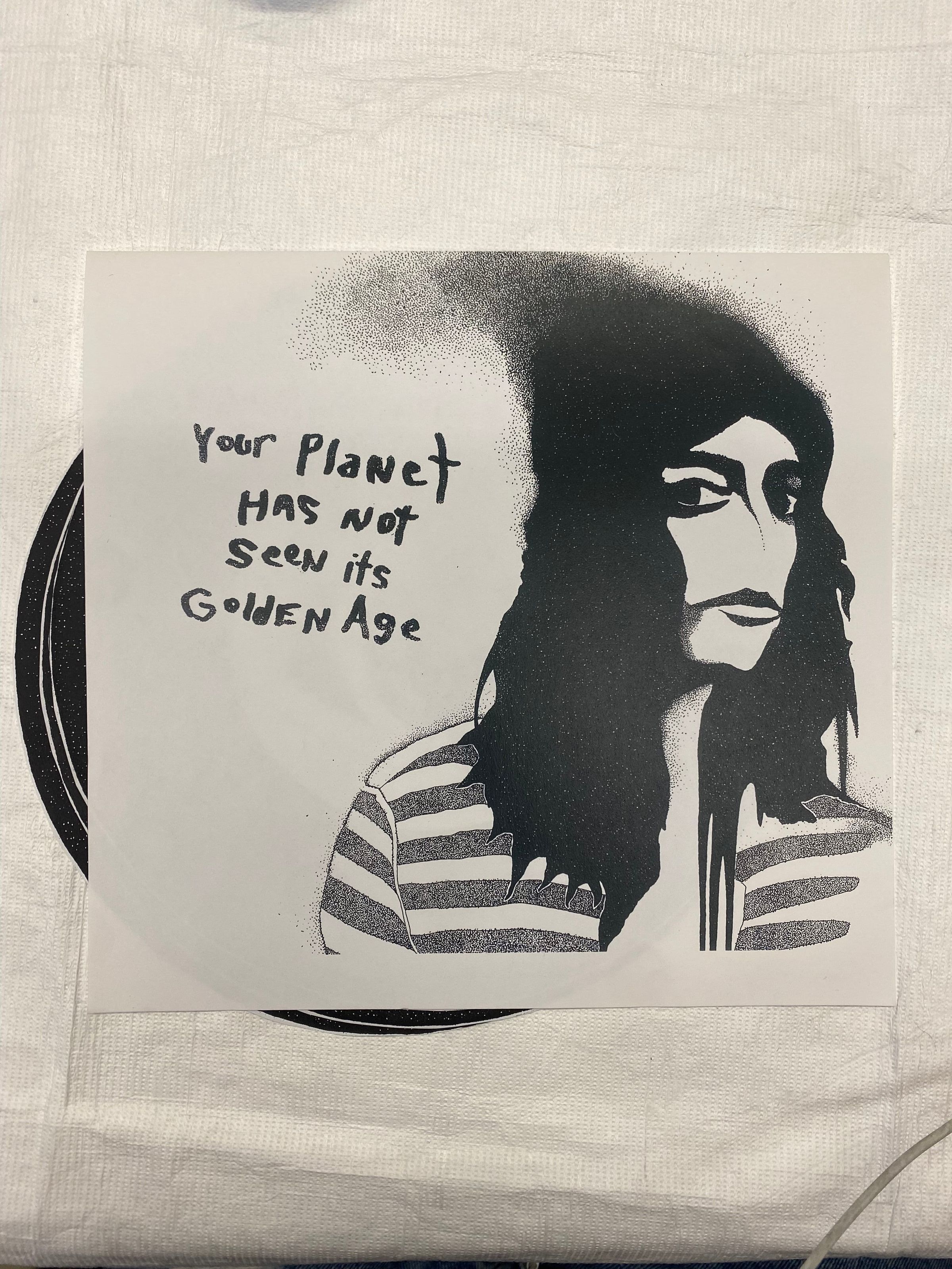 Your Planet Has Not Seen Its Golden Age (3rd Printing): Small photocopy print folded into a booklet with four internal circular prints. The external booklet on the front has a printed image of a centrally placed female figure in profile with long black hair in a striped shirt with the title of the work on the right proper. The back of the booklet contains a handwritten letter from the artist to the reader and hand-stamped text across the bottom region. Each one of the internal circular shapes includes a centrally placed motif with a black space-like border with repetitive white dots. The first image is a snake-like figure twining through the bottom of the scene, surrounded by abstracted shapes in space; above are the feet of a figure with long claw-like toenails. The second image is a female figure adorning Egyptian-style clothing and adornments, smelling a flower similar to a rose. The third image is of two canine figures in profile, one black with a white eye and one white with a black eye, with arms outstretched in the act of altercation, opposing each other like the sides of a yin-yang symbol. The fourth image is of a centrally placed eye within a rectangle with rays of light emitting below it with two snakes head down flanking either side. Beneath the eye is a pyramid with a secondary black pyramid repeated beneath it in a white square. A grid-like formation surrounds the central image.