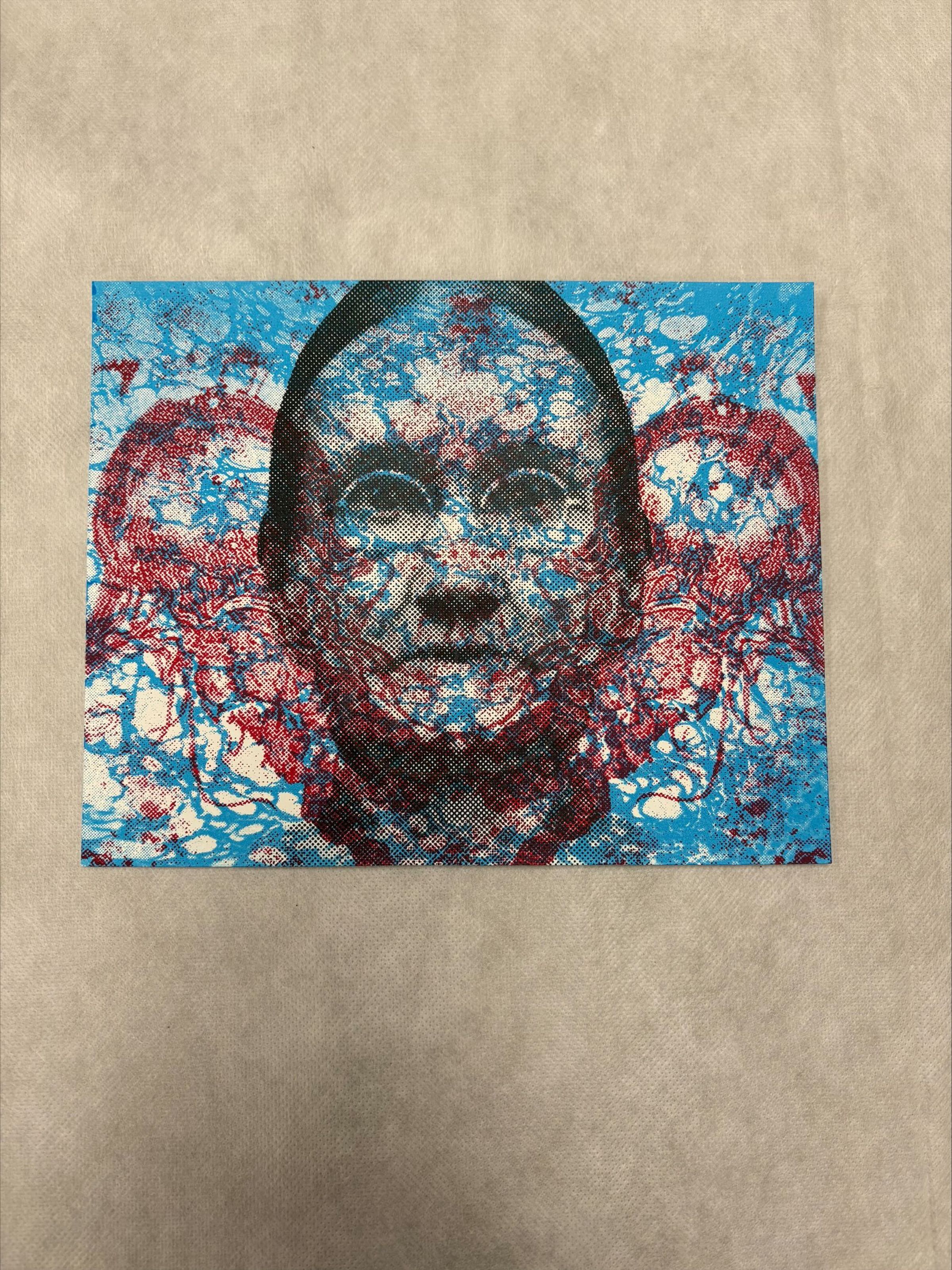 Front: A horizontally oriented, medium sized print that uses red, blue, black and white. The print is primarily of a central face that has images of water and red jellyfish overlaid on the face as the figure looks out to the viewer.