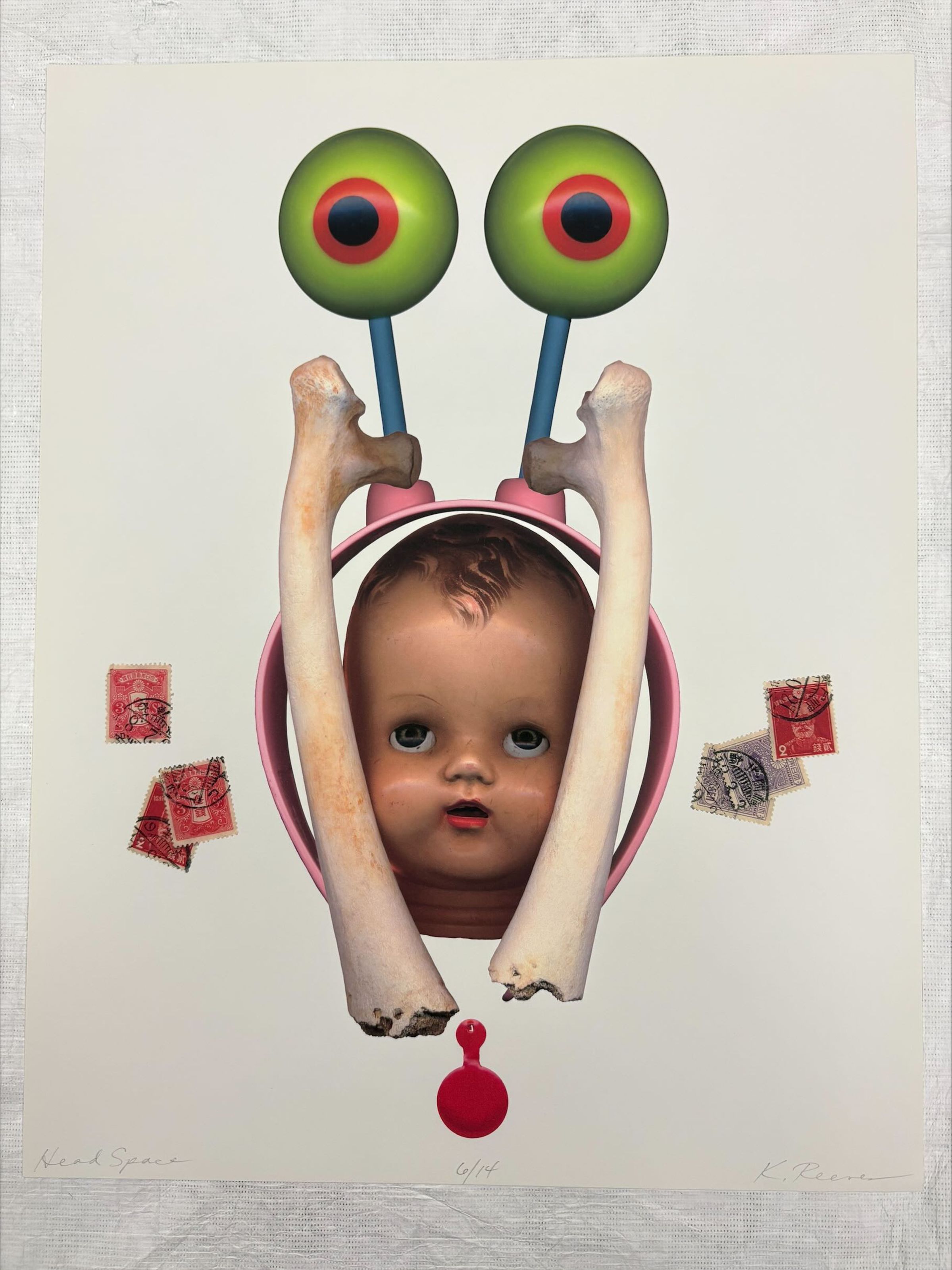 Front: A vertically oriented, medium sized print that utilizes multiple colors and references to pop culture. The prints central subject is that of a decapitated baby doll head flanked on both sides by bones and over top is a headband like object depicting the eyes of a cartoon snail. An off to each side of the central scene are blue and red playing cards.