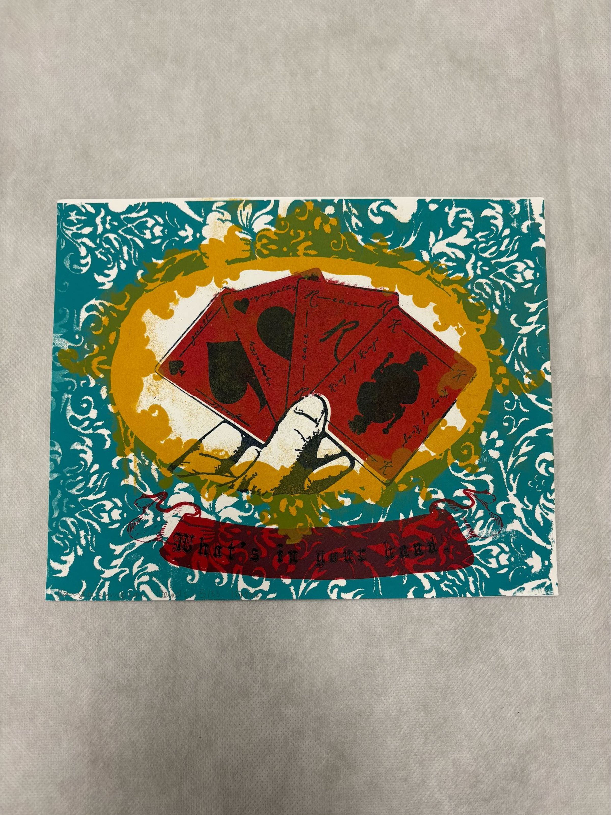 Front: A horizontally oriented, medium sized print that utilizes red, yellow, blue, black and white to create the imagery of the print. The composition of this print is made up of a central arrangement of playing cards being held in a hand and around it there are organic floral like patterns in blue and yellow.