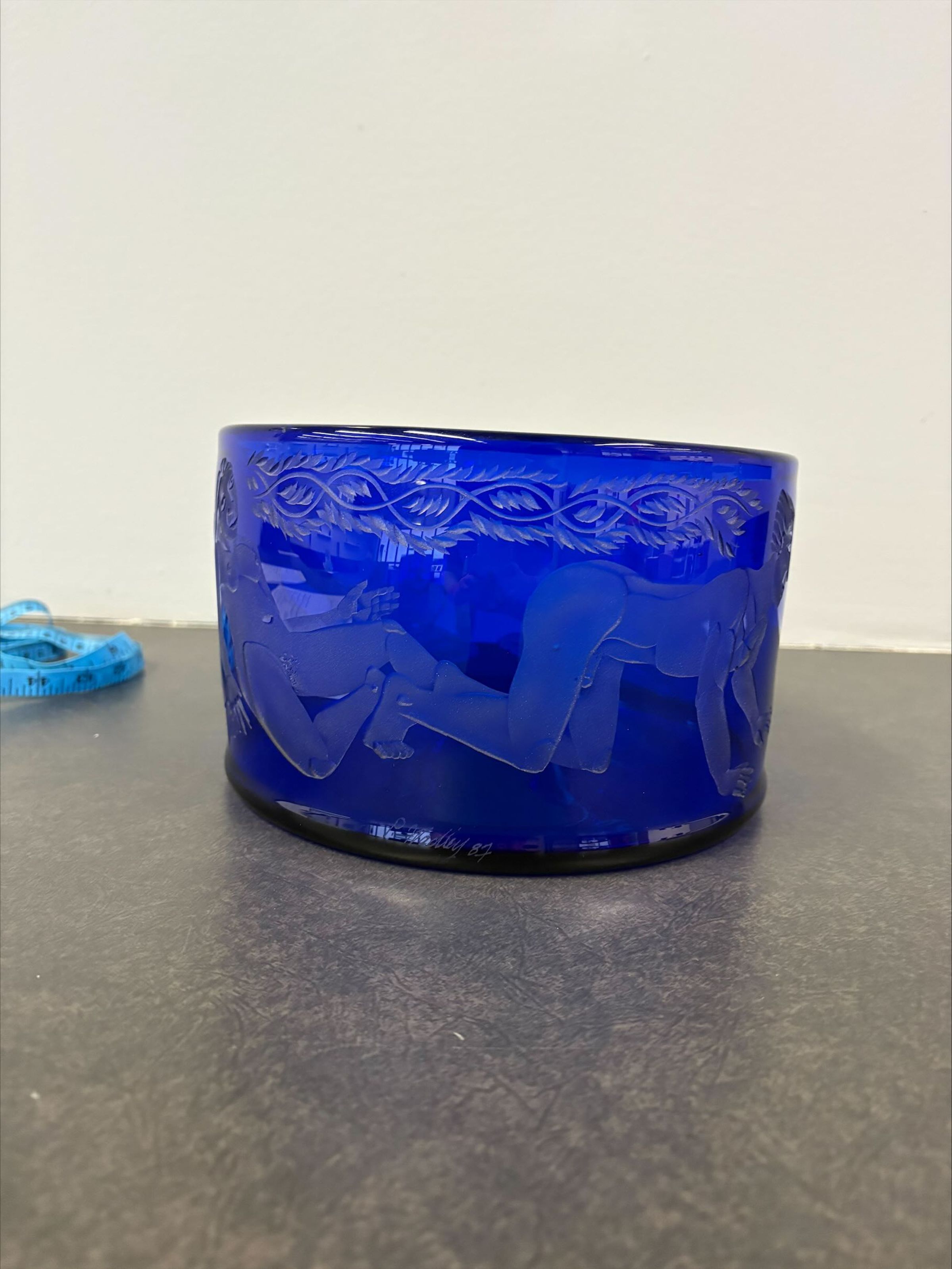 Cobalt Blue Bowl: A small cobalt blue glass bowl with several sand-etched nude female and male reclining and kneeling figures. Along with the figures that travel around the entire body of the bowl there are also vine like details that travel above them.
