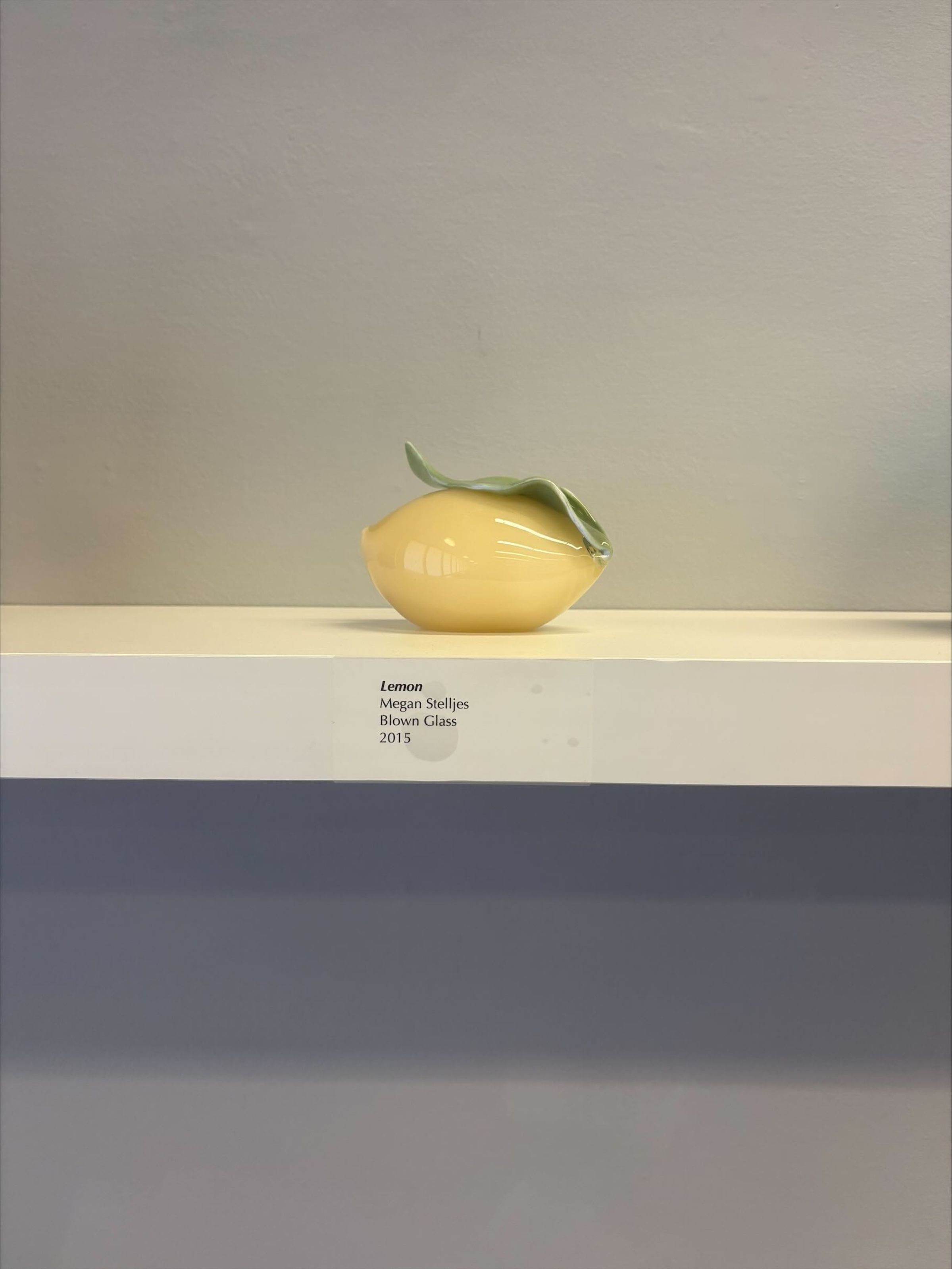 Lemon: A small hand-blown glass lemon with leaf accent attachment to the top. The lemon itself is a butter yellow color, while the leaf that curls upwards at the top is a light green color.