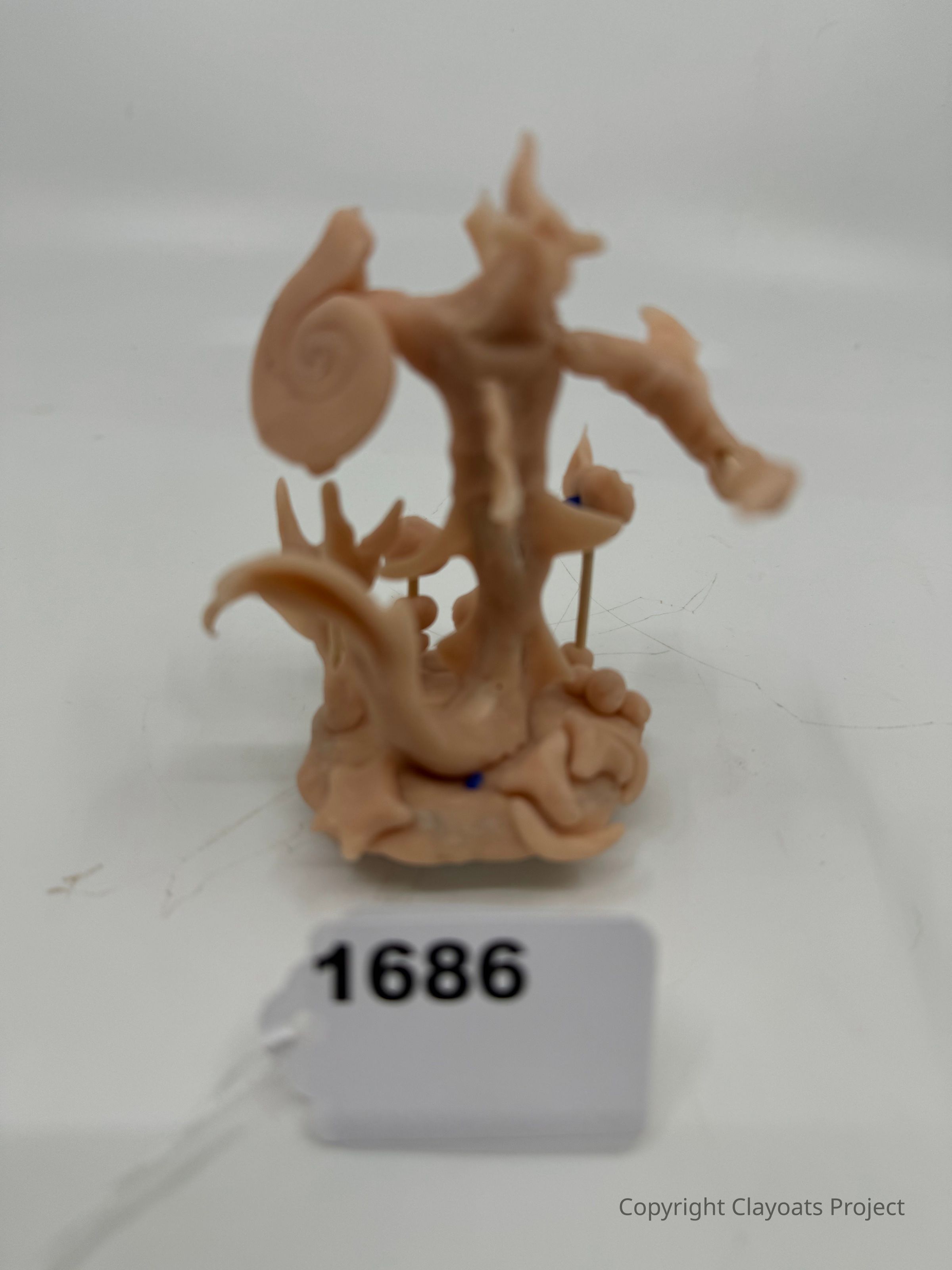 The image shows a small, intricate sculpture made of a beige material, featuring a figure with distinct swirling and organic shapes that resemble a mythical or fantastical creature, set against a plain background; and the overall composition conveys a sense of artistry and imagination in its design.