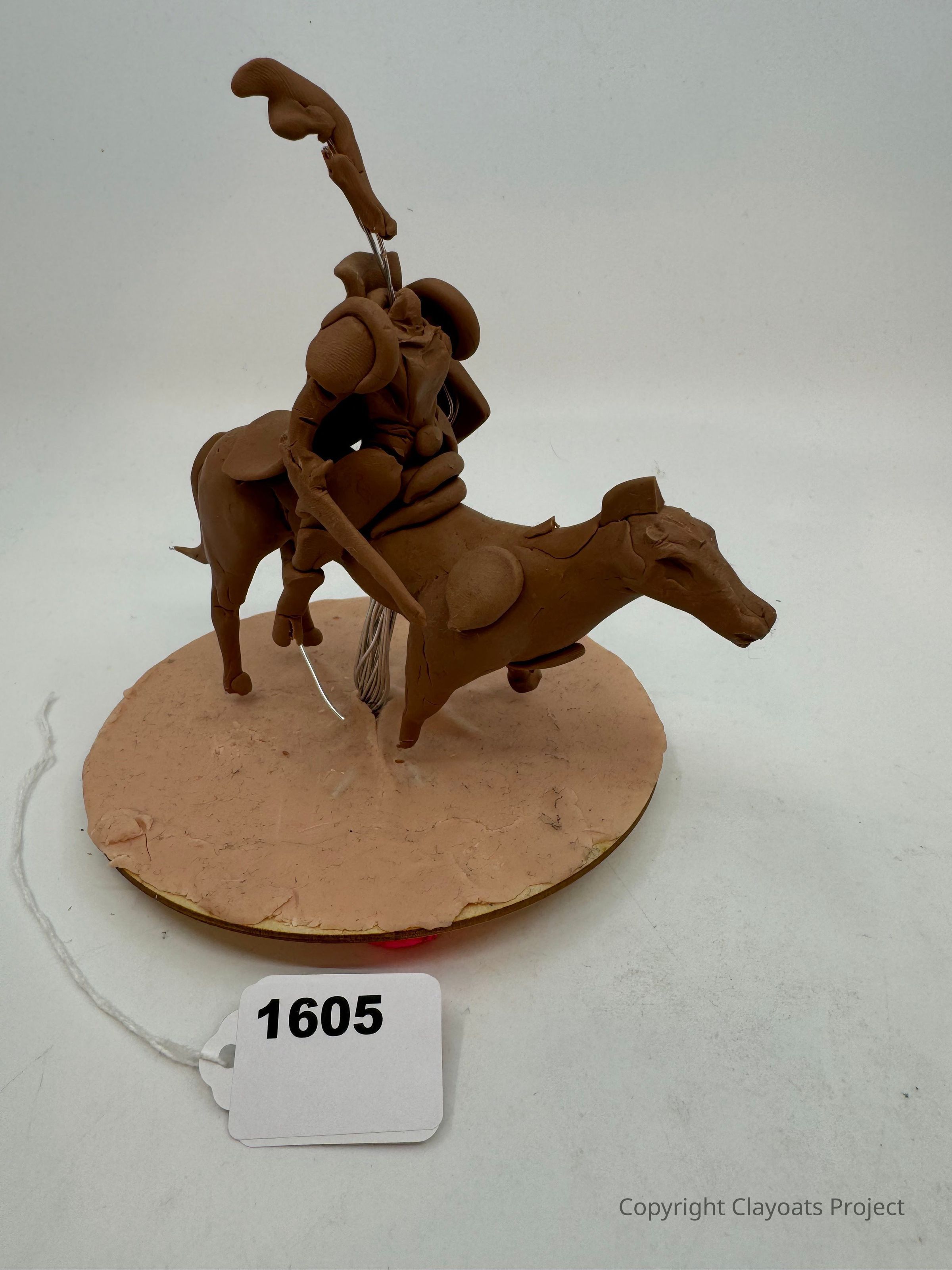The image shows a handcrafted sculpture made from brown clay, featuring a knight in armor mounted on a horse. The knight is leaning forward, holding a lance upright, as the horse stands on a circular base. The sculpture's details, such as the knight’s armor plates and the horse’s mane, are intricately crafted, capturing a sense of motion and readiness. . The background is plain, highlighting the artistry and complexity of the piece.