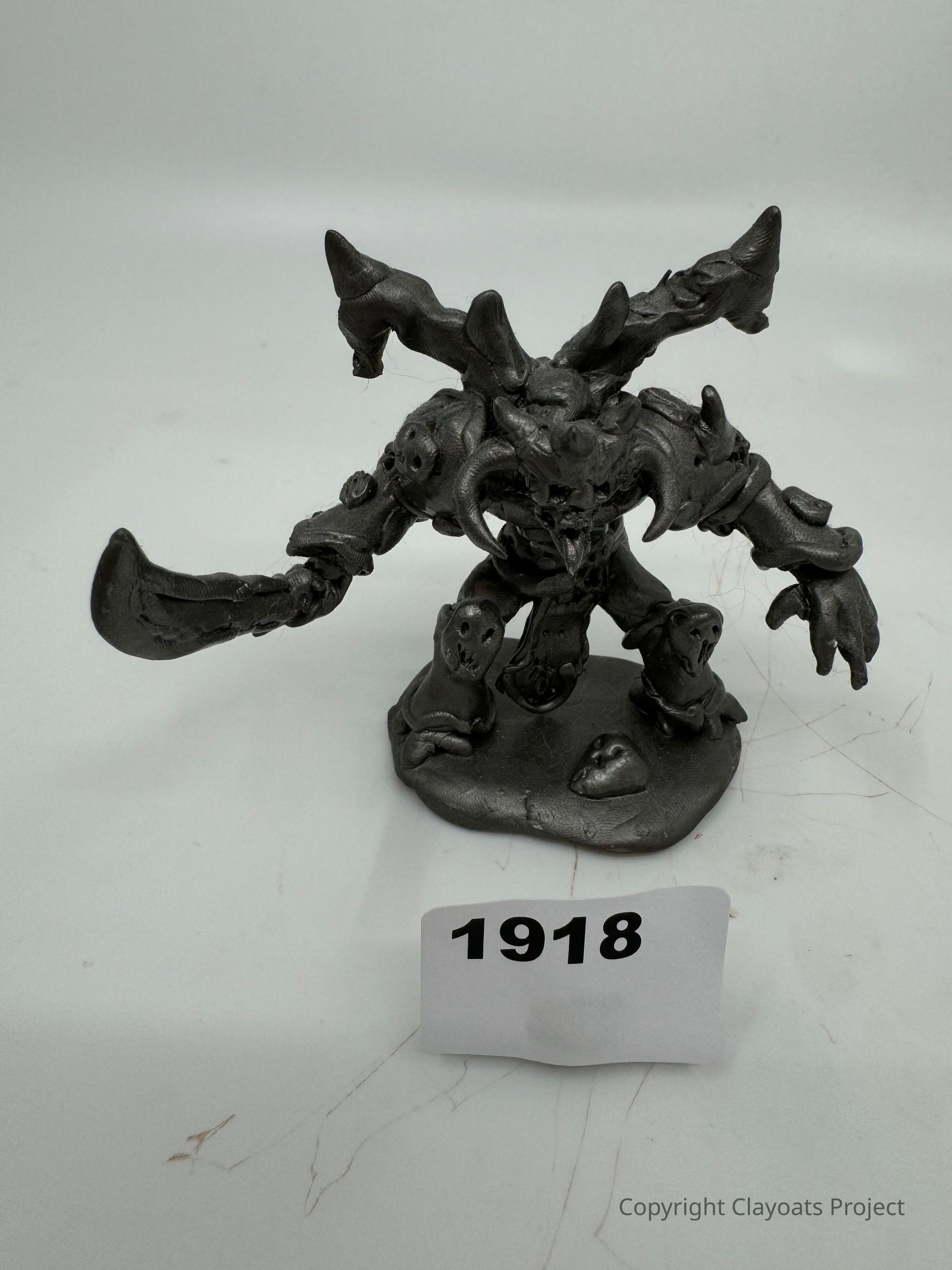 The image showcases a detailed metallic sculpture of a fantastical creature with horned appendages, exaggerated features, and a large, curved weapon-like arm, all positioned on a base, likely representing a character from a fictional universe. The creature's design includes various intricate elements like spikes and armor, emphasizing an aggressive and intimidating appearance, and is set against a