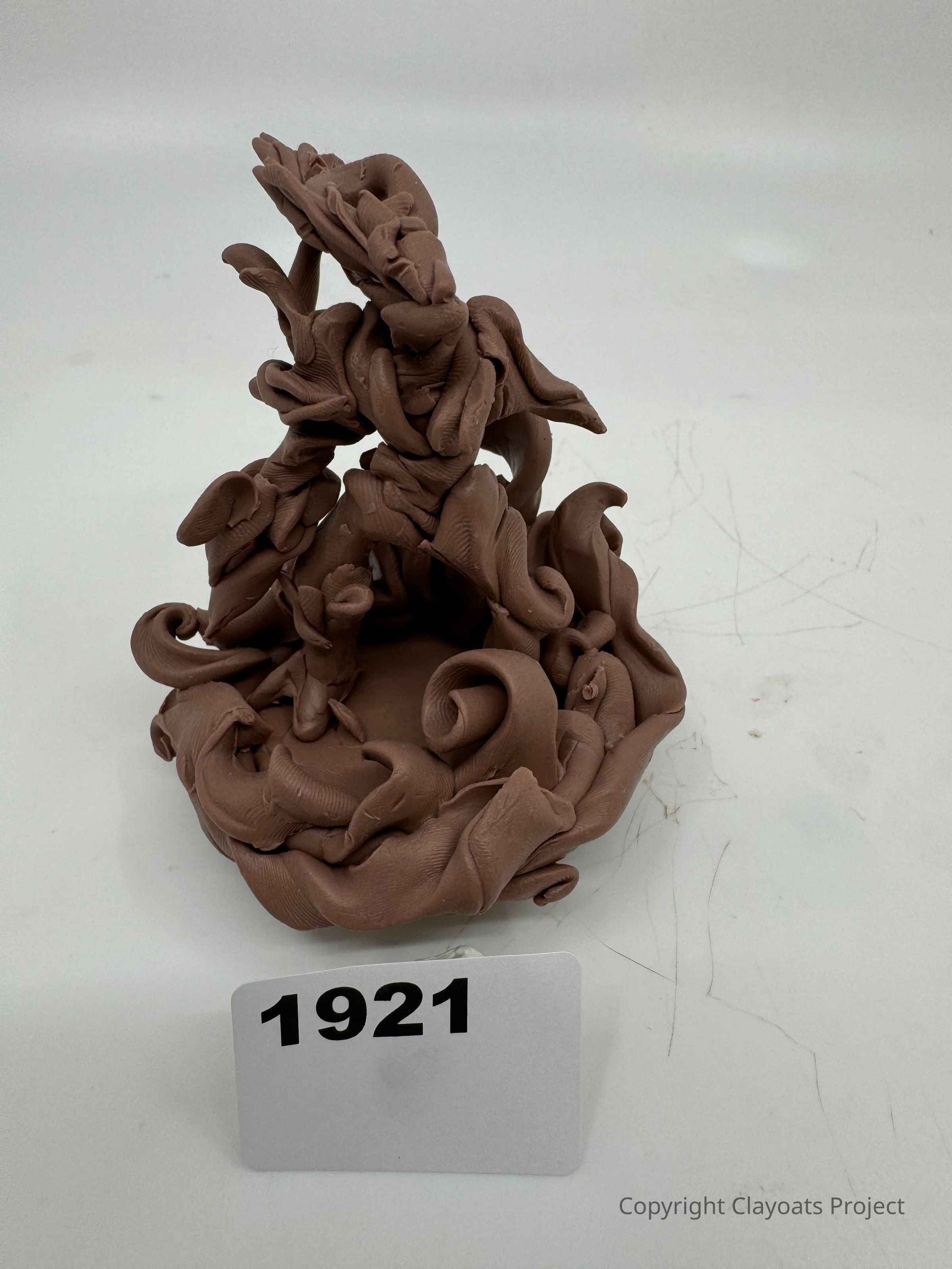 The image features a clay sculpture with an intricate and abstract design, showcasing a series of flowing and twisting shapes that appear almost organic in nature, resulting in a visually captivating piece that invites various interpretations; which is set against a neutral background, emphasizing the sculpture's rich texture and details.