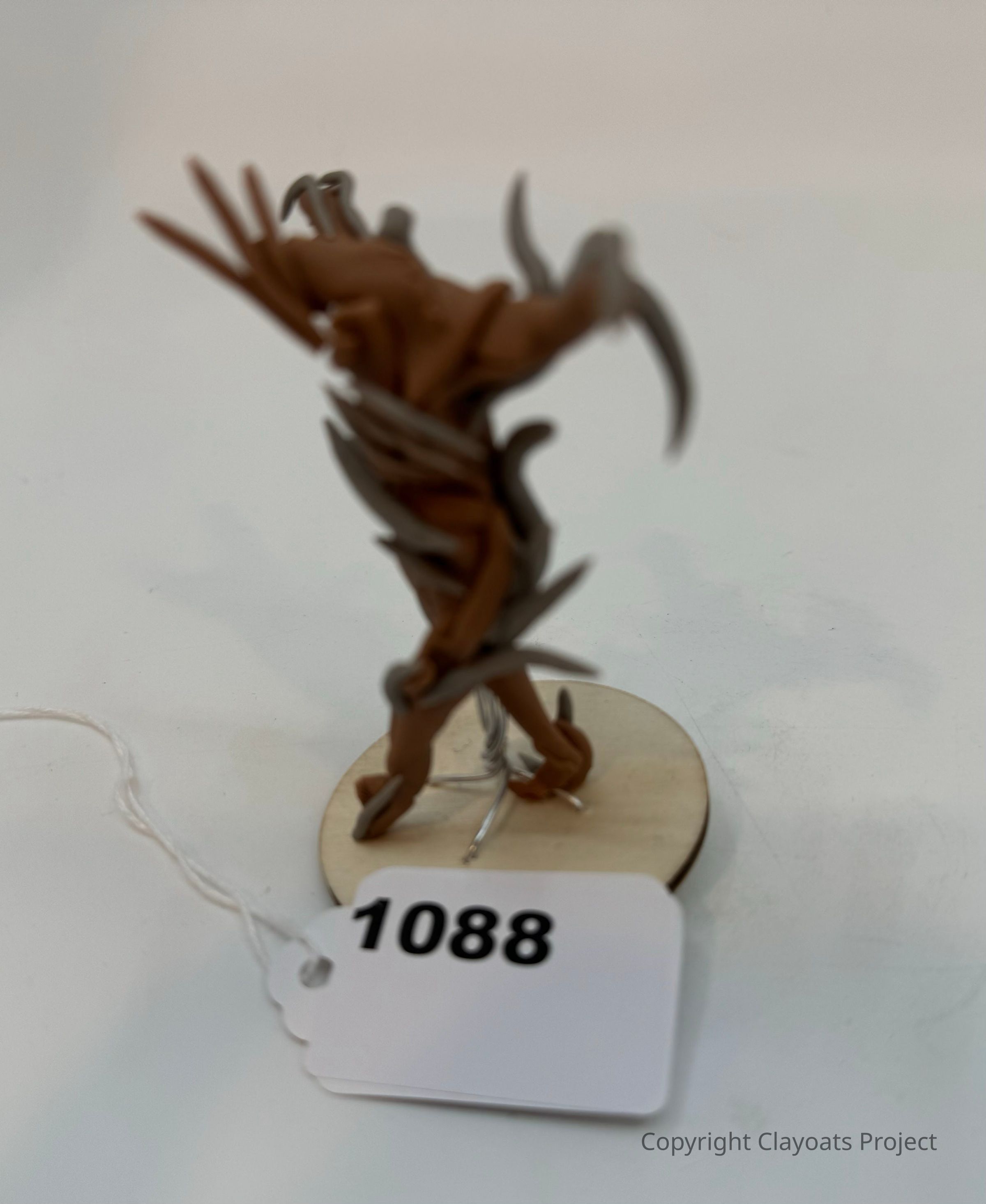 The image depicts a small, intricately detailed figurine that appears to be a creature with elongated, claw-like limbs and a dynamic pose, suggesting movement or action. The figure's design has elements that seem to mimic organic, spiky armor or appendages, giving it a menacing or formidable appearance set against a plain background.