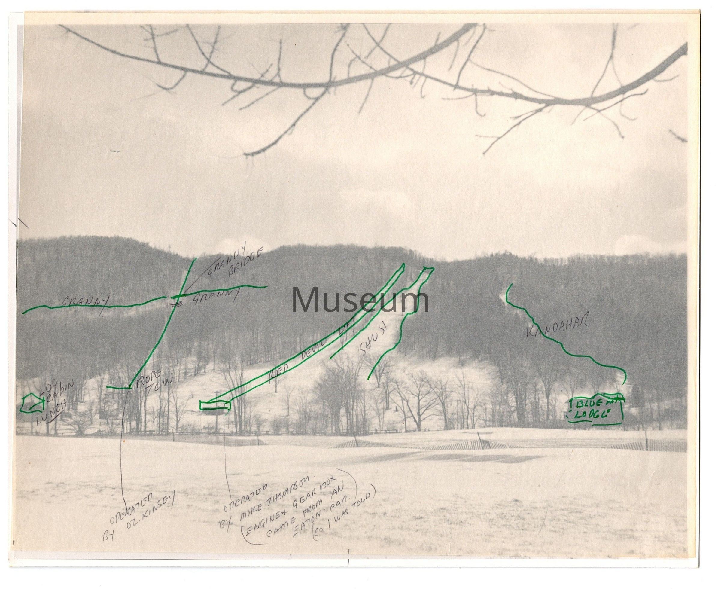 Blue Mountain Ski Area with overlay: Black and white photo of the Blue Mountain Ski Hill with a light brown overlay indicating more details about the name of the hills and the lifts found on the hills. The photo is taken of the portion of Blue Mountain that is now known as “North”. The overlay has green pen marks indicating important information regarding the hills in the photo. Starting from left to right, there is a small house drawn in green pen in the bottom left hand section with writing that reads “ Log Cabin Lunch”, right above it are two intersecting green lines that read “ Granny” on either side of the intersection, the actual intersection reading “Granny Bridge” and a small green line pointing towards the left reading “Rope Tow”. There is a pencil drawn line to the “Rope Tow” that reads “Operated by Oz. Kinsey”. Beside the Rope Tow are two more green lines indicating the cable lines for the “Red Devil Lift” which also has a pencil addition towards the bottom of the photo that reads “Operated by Mike Thompson (Engine and Gearbox came from as Eaton Car. So, I was told). Next to the ski lift is a green outline for the hill labeled “Shush” and on the far right side is a smaller outline labeled “Kandahar” which leads to another small green building labeled “ Blue Mountain Lodge”.