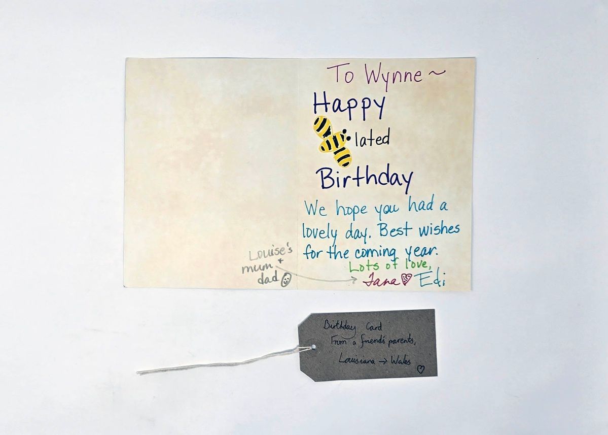 An opened belated birthday card to Wynne from Jane and Edi. The "B" of Belated is stylised as a Bee. With a brown, handwritten luggage tag.
