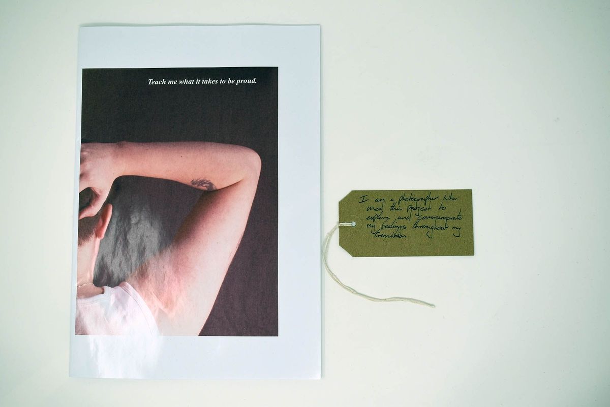 Booklet entitled "Teach me what it takes to be proud." The cover image is a close up of someone raising their right arm, taken from behind. Also a brown, handwritten luggage tag.