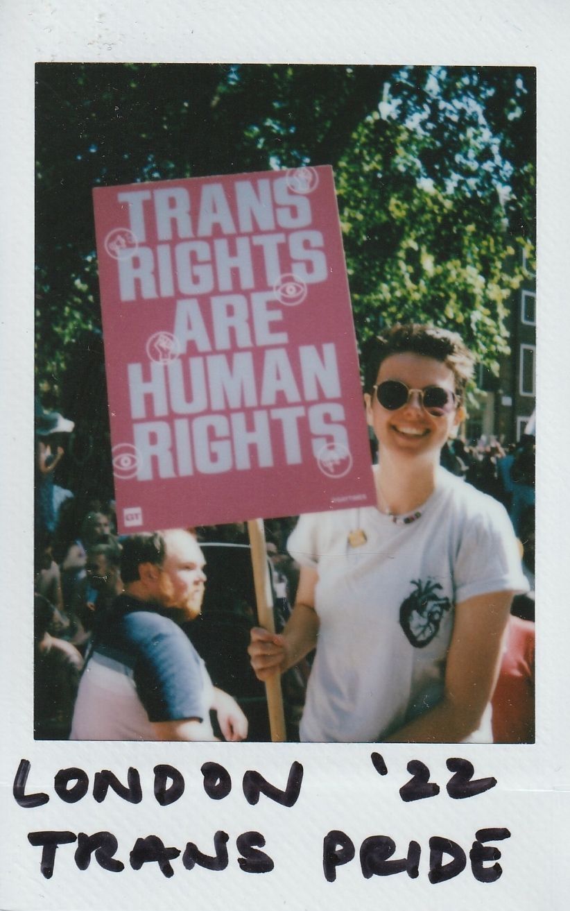 A person smiling and holding a sign which says "Trans Rights Are Human Rights".