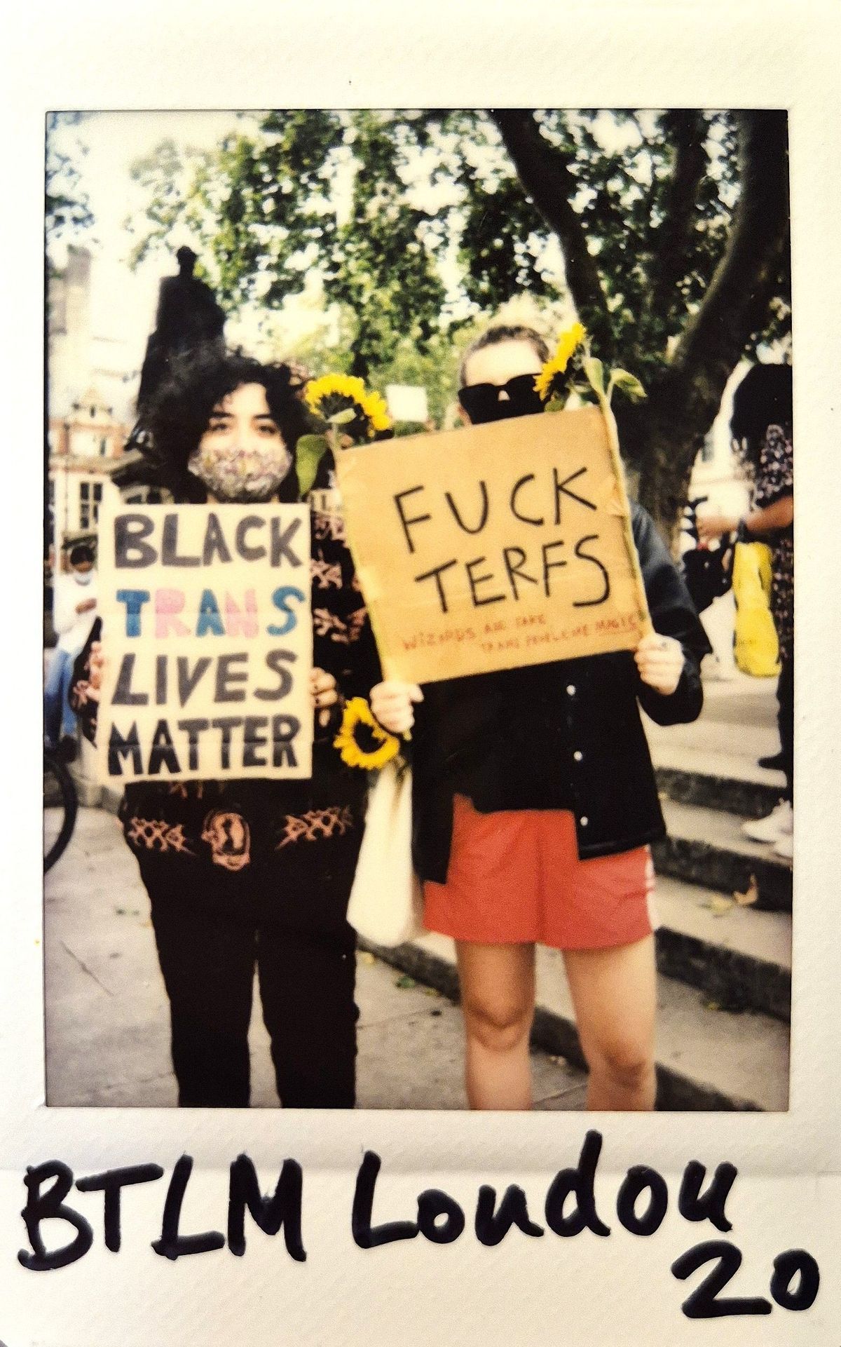 Two individuals stand outdoors holding protest signs advocating for Black trans rights and opposing TERFs.