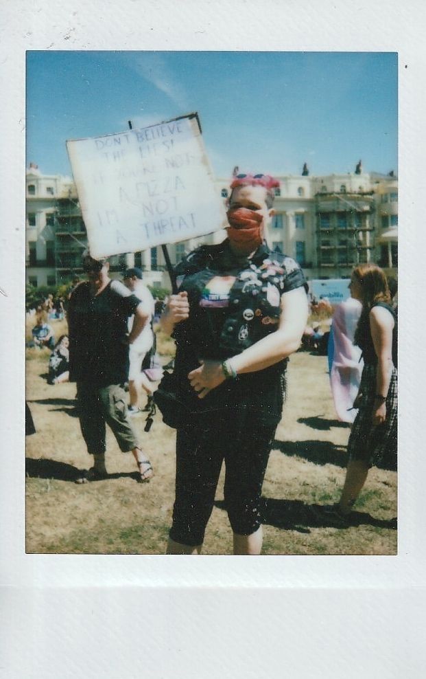 A person with pink hair holds a sign which has a message that is too blurry to make out.