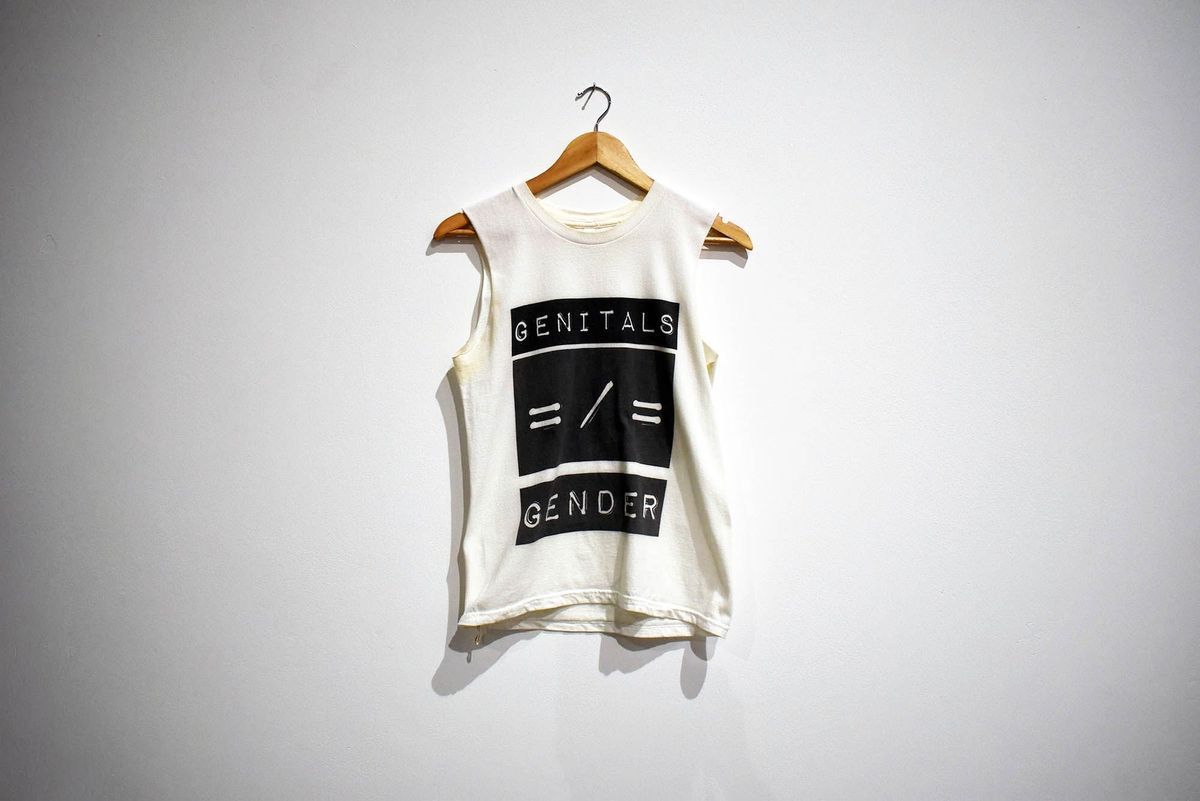 White t-shirt with sleeves cut off. Three black boxes on the front with white text reading "Genitals" "=/=" "Gender"