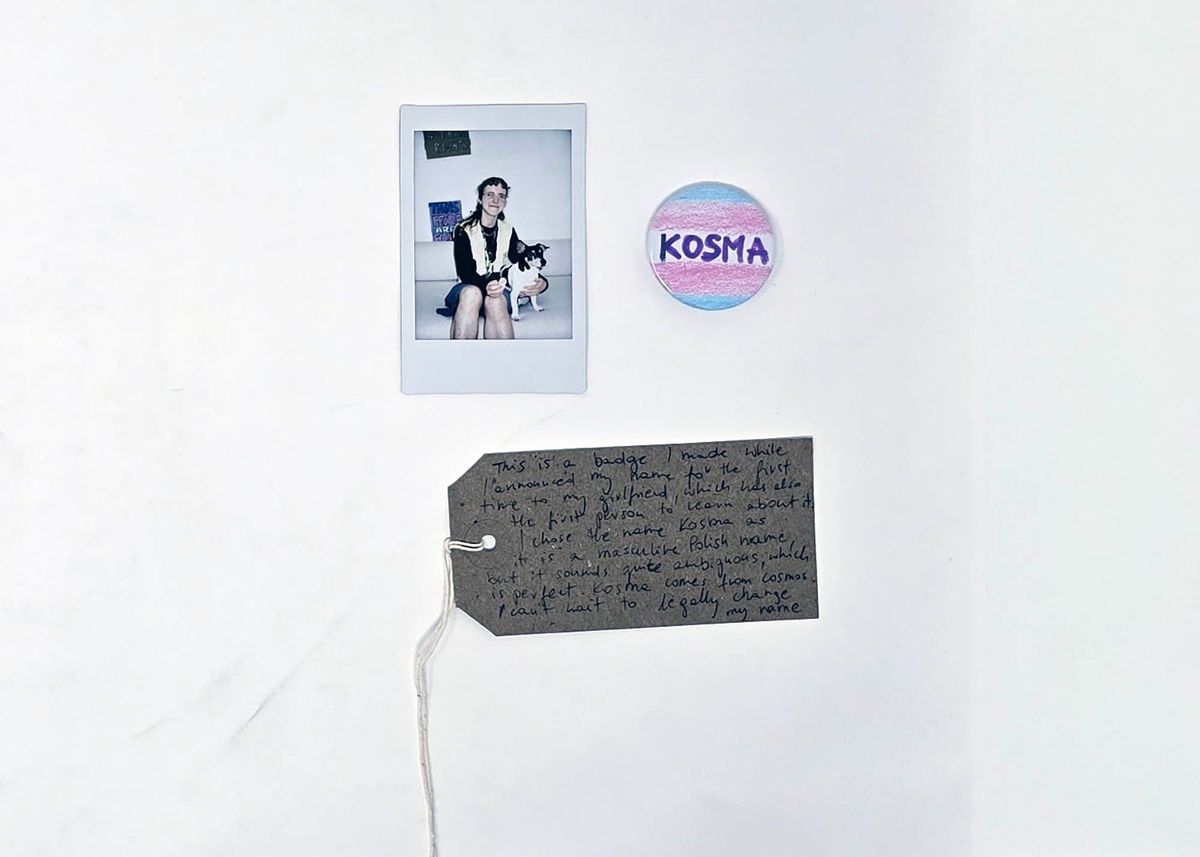 A small badge coloured in the trans flag colours and featuring the name "KOSMA". With a Polaroid of the donor and a brown, handwritten luggage tag.