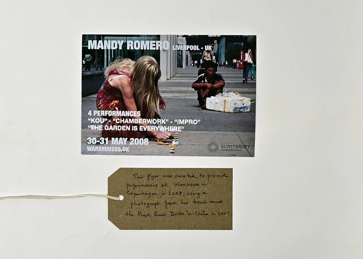 Promotional flyer for a Mandy Romero event in Liverpool. The images is of a person with long blonde hair, in a red dress squatting down. With a brown, handwritten luggage tag.