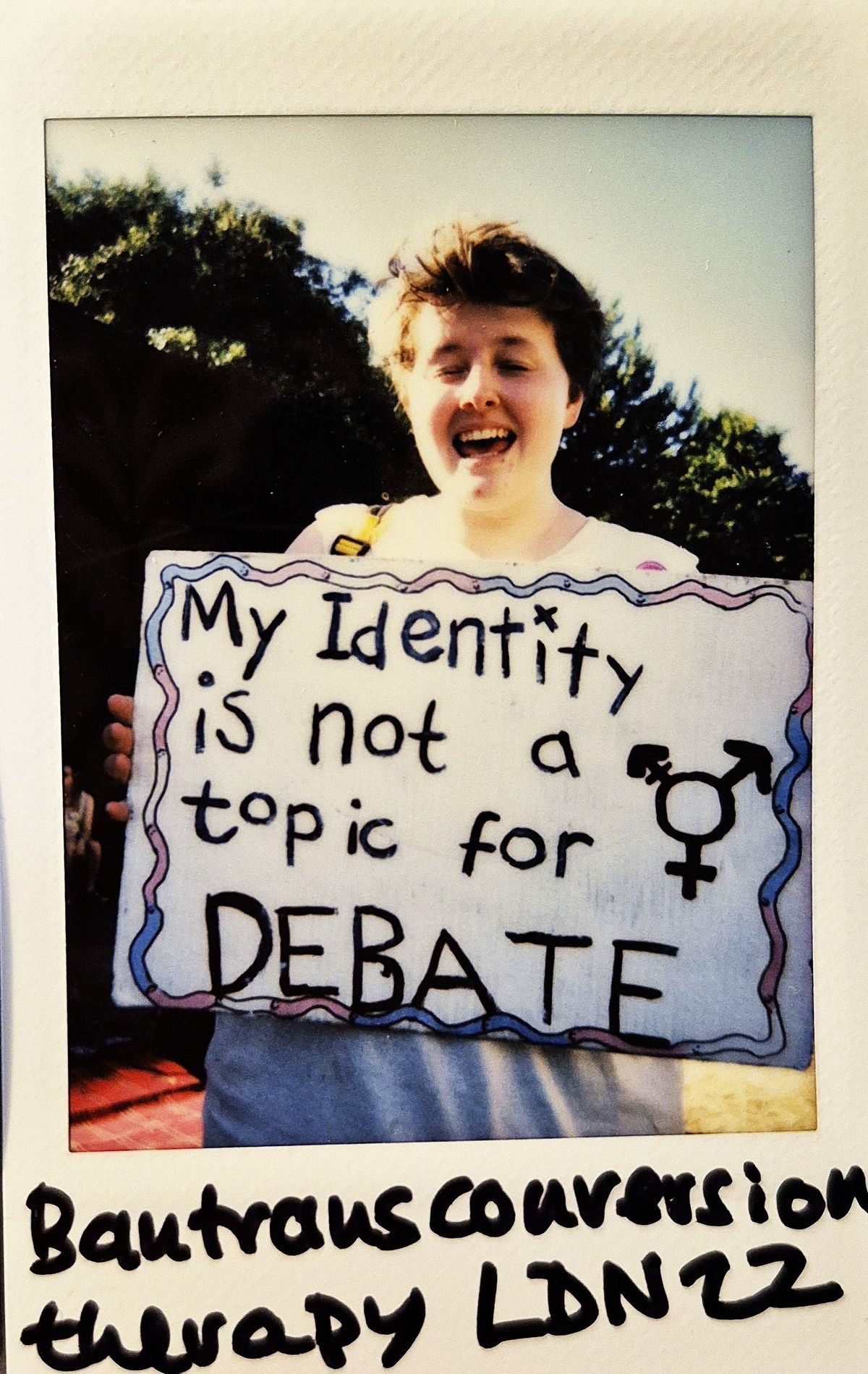 A person holds a sign reading "My Identity is not a topic for DEBATE".