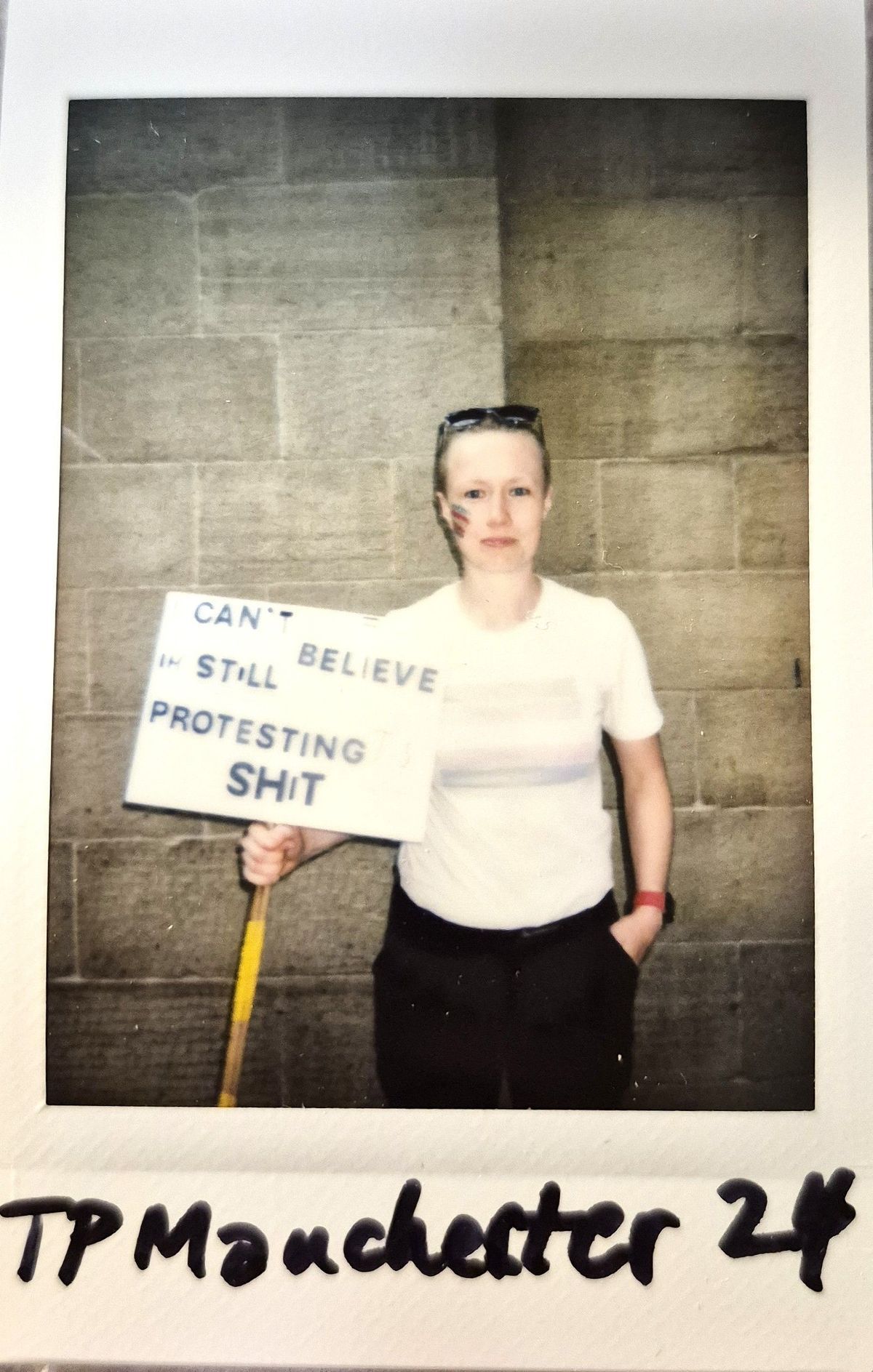 A person stands holding a sign reading, “Can’t believe I’m still protesting this shit,".