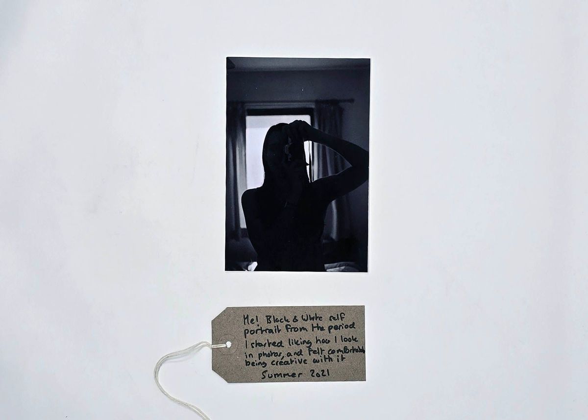 A black and white photo self-portrait/silhouette photo taken in a mirror. With a brown, handwritten luggage tag.