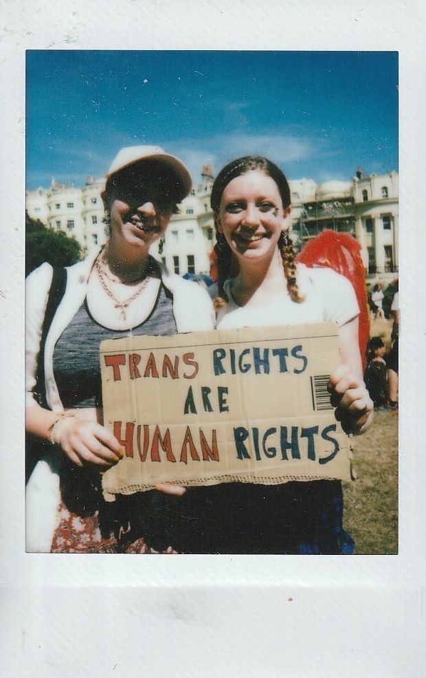 Two smiling individuals stand outdoors holding a sign that reads "Trans rights are human rights."