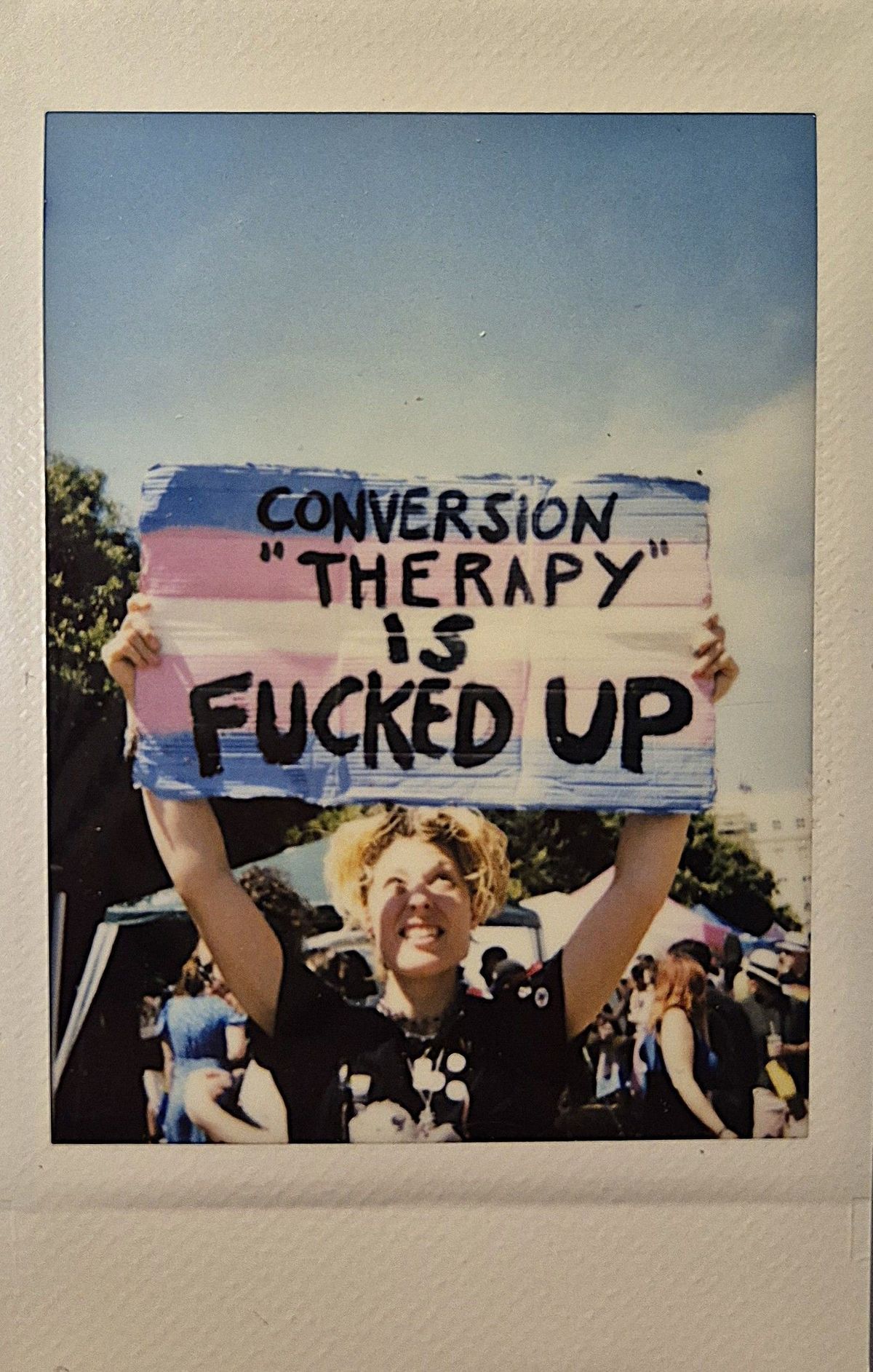 A person holds a sign which says "CONVERSION THERAPY IS FUCKED UP".