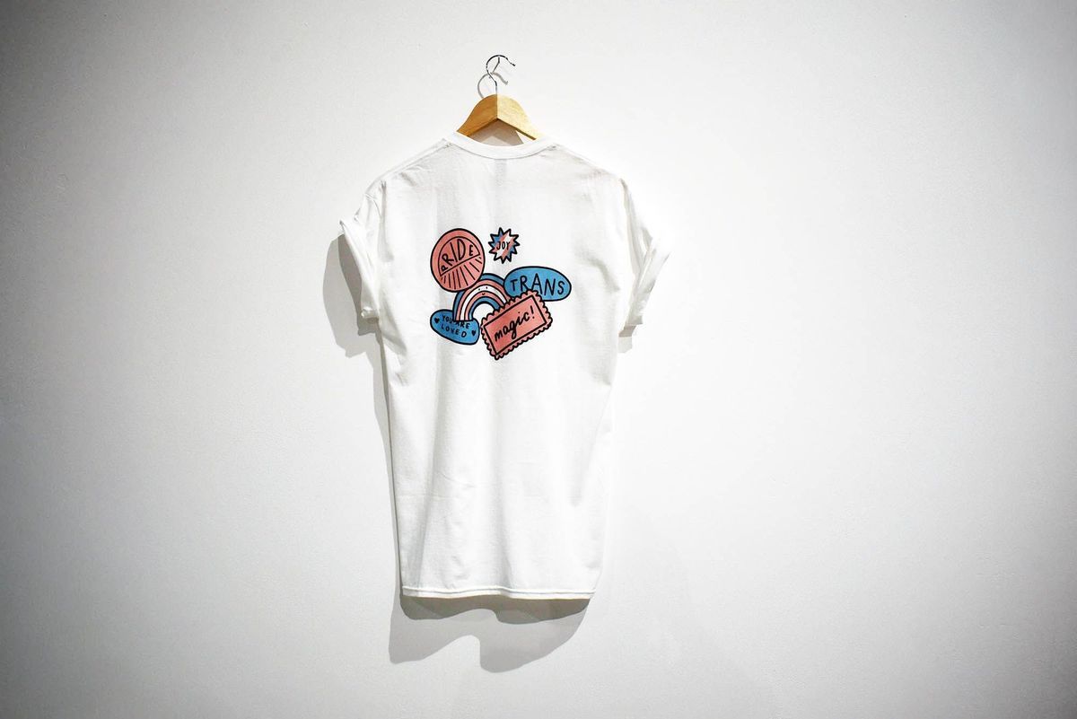 A white t-shirt with colorful illustrations and positive messages hangs on a wooden hanger.