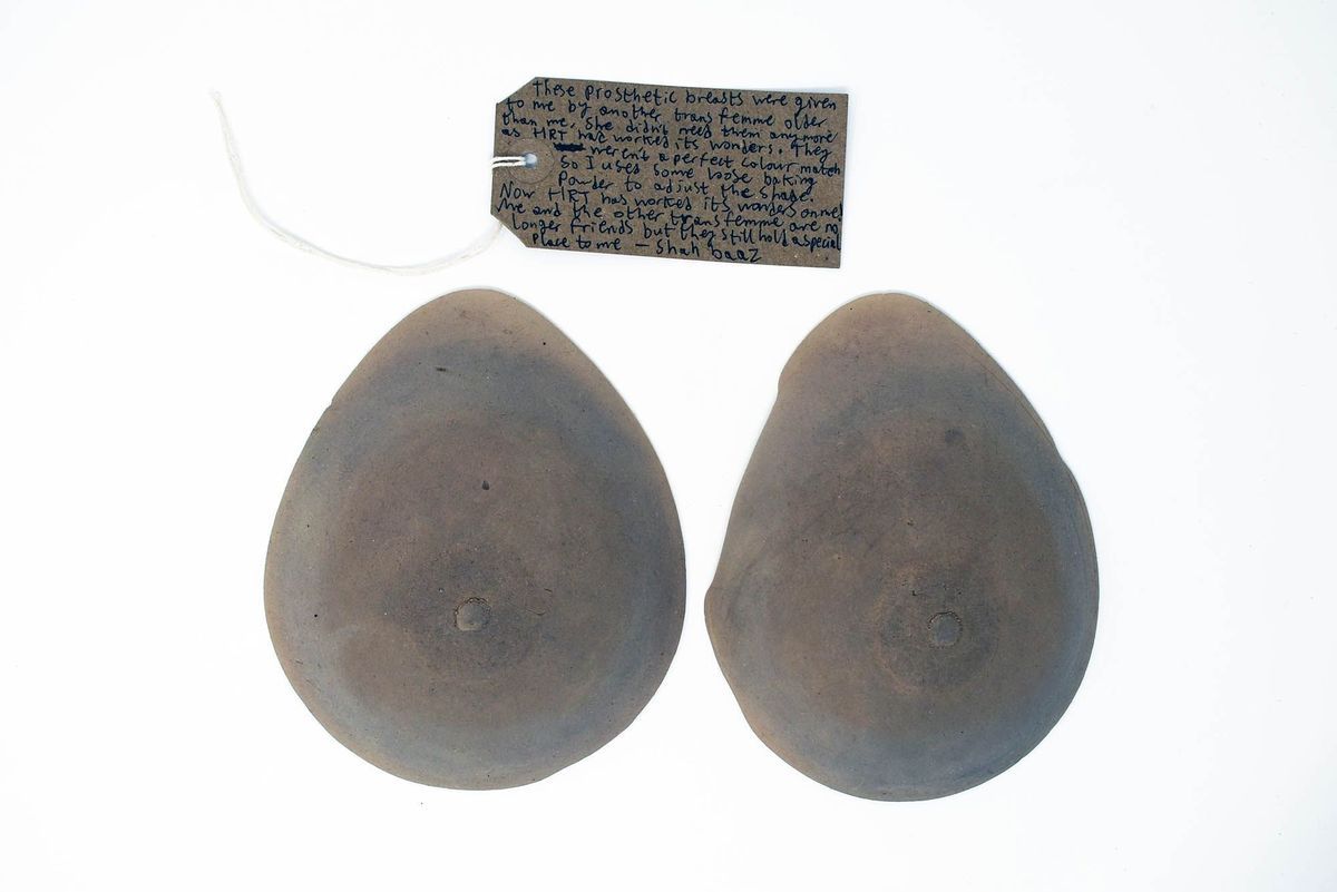A pair of teardrop shaped breast forms, slightly discolored. With a brown hand written luggage tag.