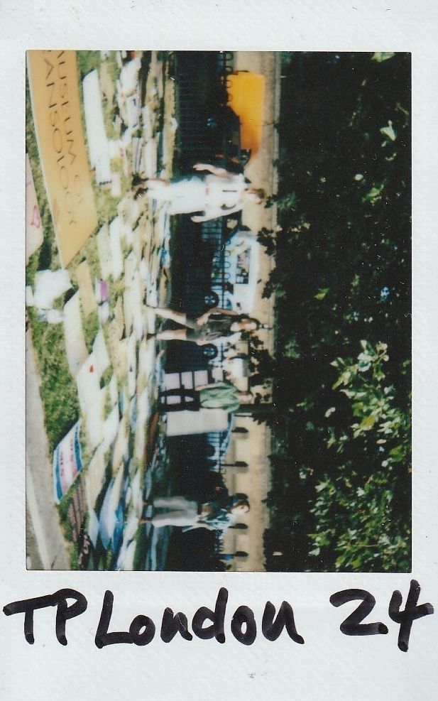 The image shows people standing near a fence with lots of placards laid on the ground beside them.