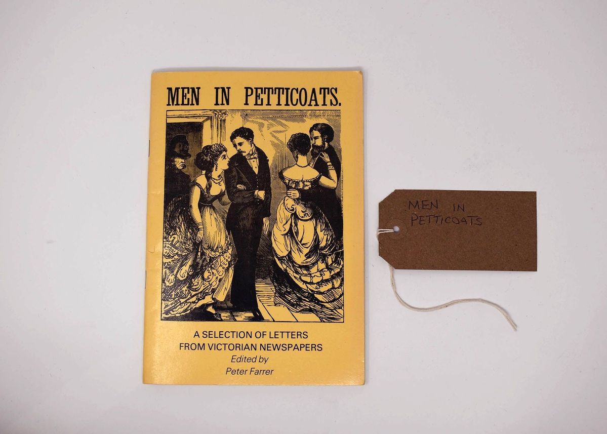 A yellow book which is called 'Men in Petticoats' which has an illustration of a several couples of people dressed in suits and dresses dancing.