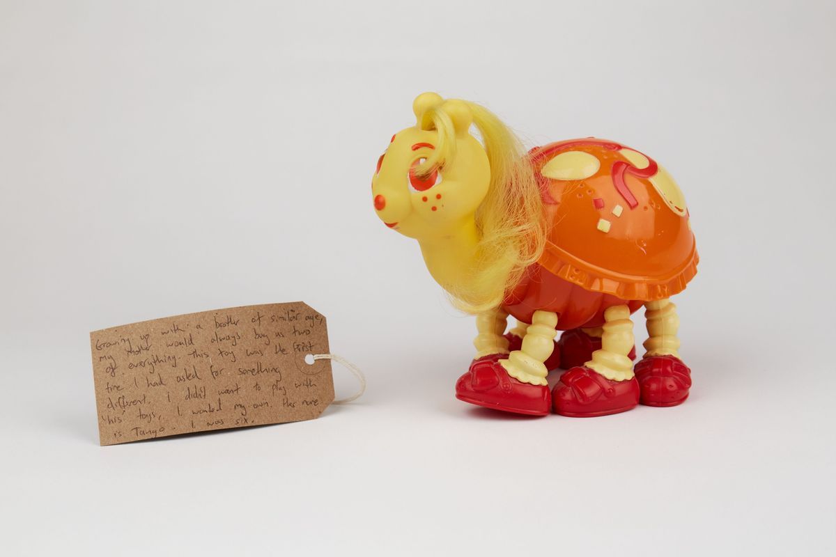 A children's toy which is a ladybug that is yellow and has an orange/red shell. It has hair on it almost like a my little pony. There is also a brown luggage tag  with writing on.