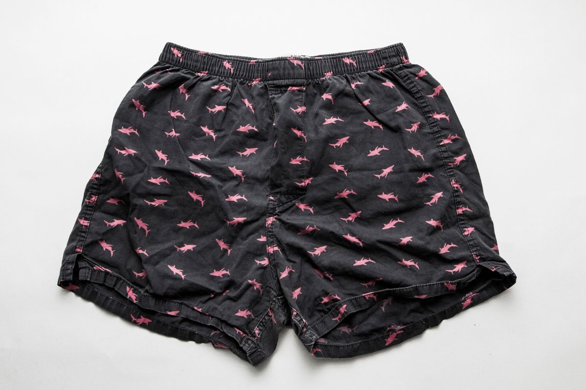 A pair of dark blue boxer pants with a pattern of pink shark silhouettes