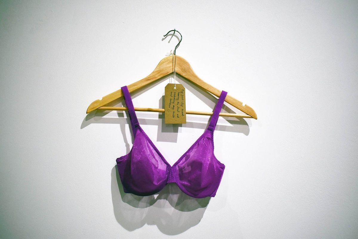 A fushia bink unpadded bra, with a glitter sheen to surface on a wooden hanger. Also, a brown, handwritten luggage tag.