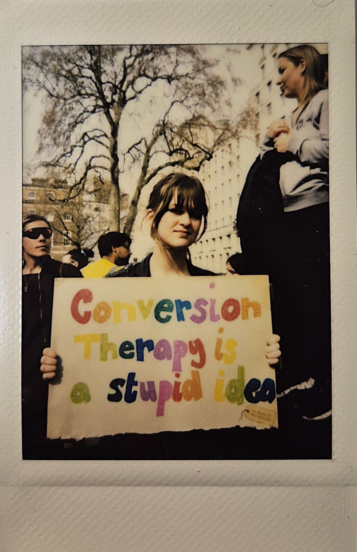 A person holds a colorful sign reading "Conversion Therapy is a stupid idea" during a protest.