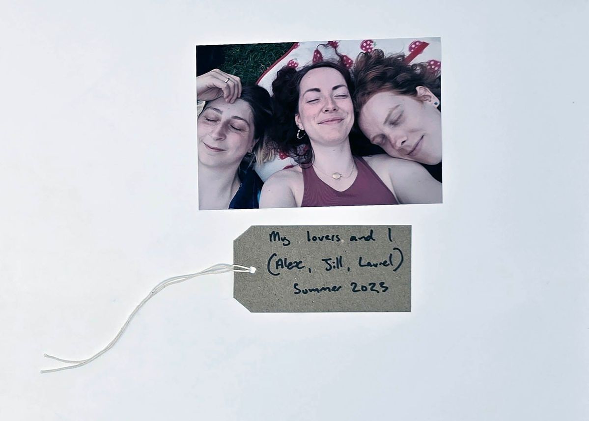 Close up photo of three peoples faces as they lie on the ground with their eyes closed. With a brown, handwritten luggage tag.