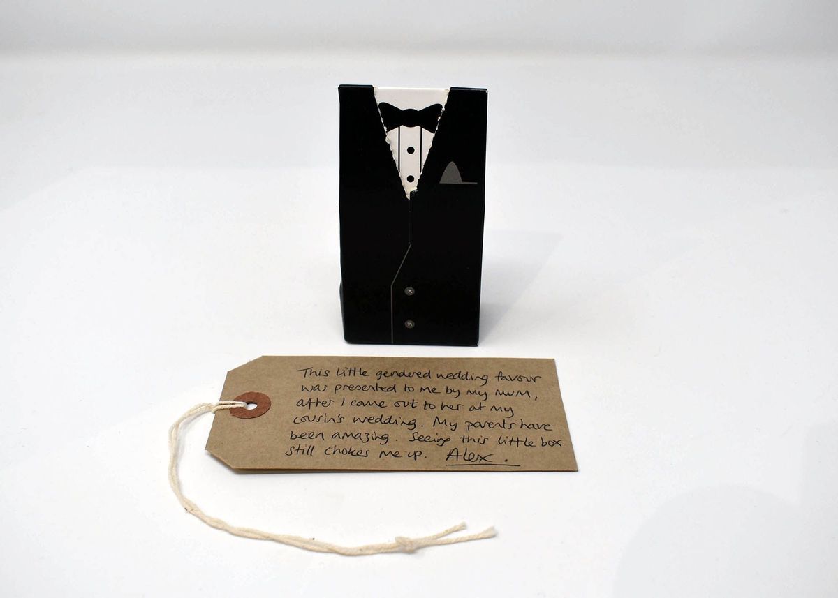 Small black box made out of card, patterned like a tuxedo. There is a small white string coming out of the top right corner of the box.