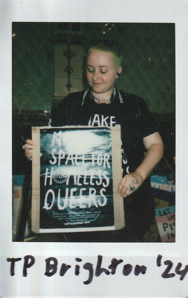 A person holds a poster advocating for "space for homeless queers".